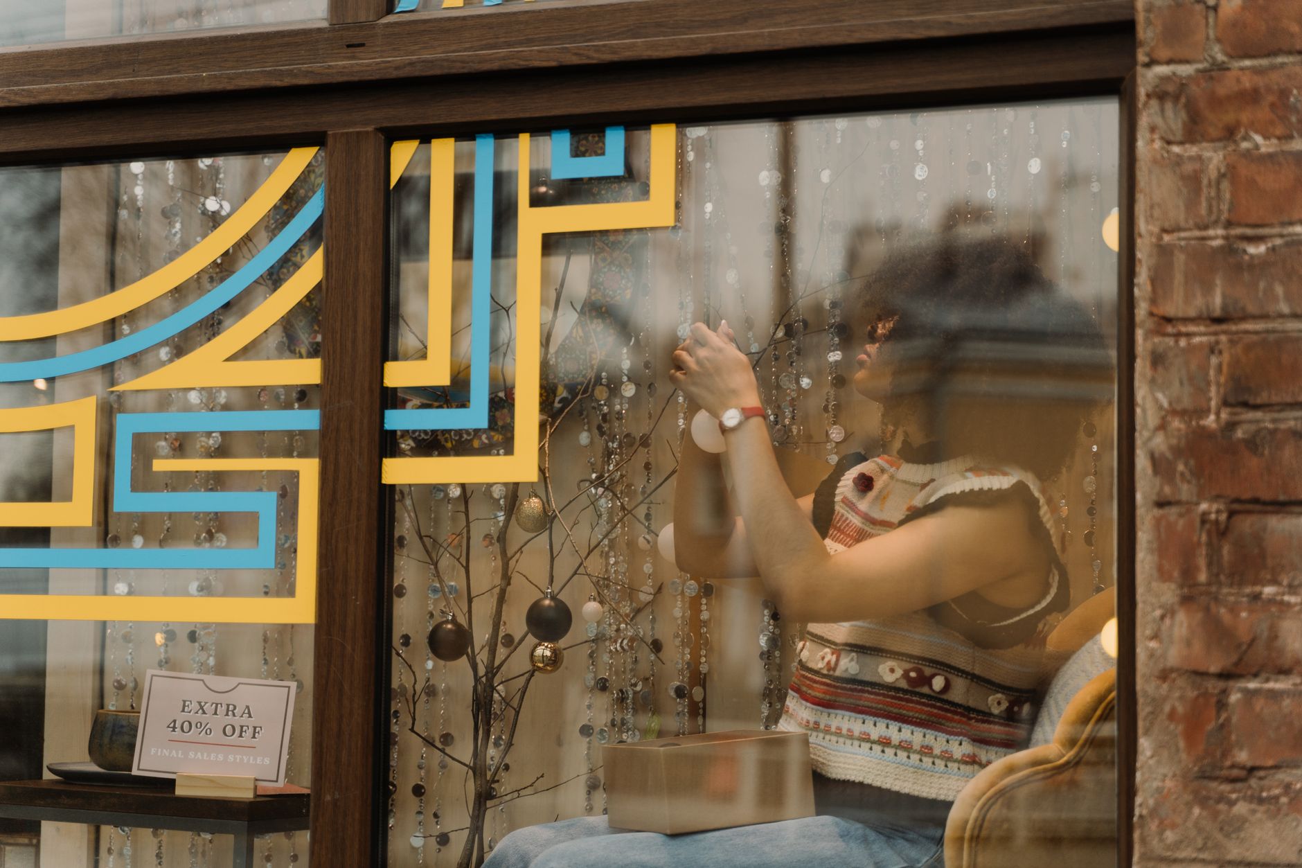 A woman decorates a store window with holiday decorations, offering a cozy and festive ambiance.