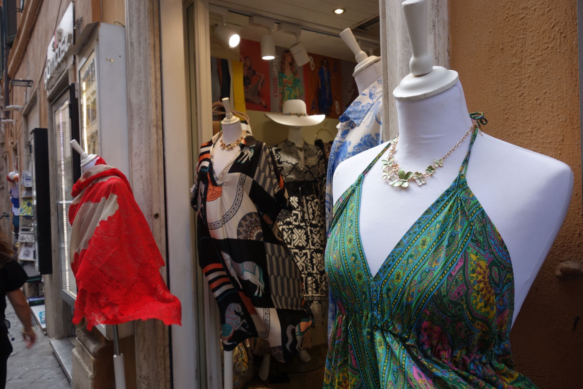 Mannequins adorned with colorful summer dresses and scarves in a boutique display window.