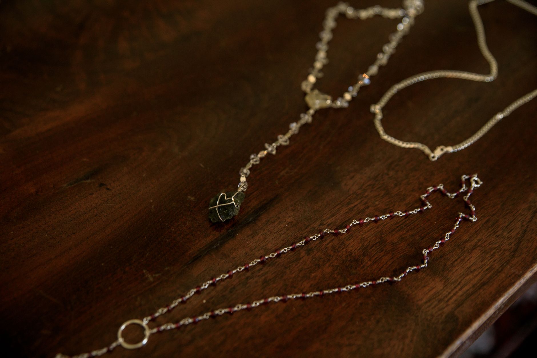 Close-up of elegant silver and gemstone necklaces elegantly laid on a dark wooden table.