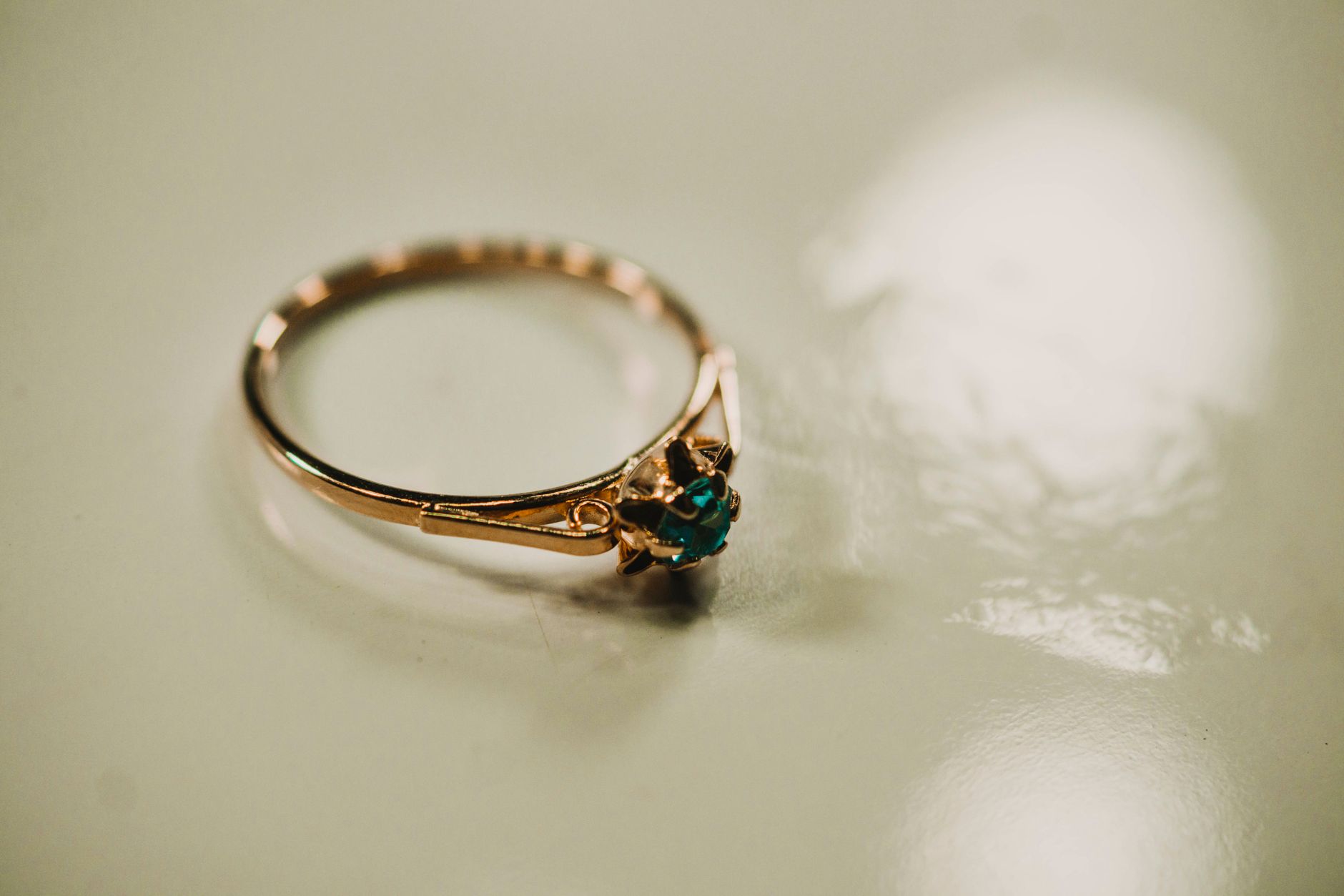 Close-up of a delicate gold ring with a green gemstone reflecting light on a smooth surface.