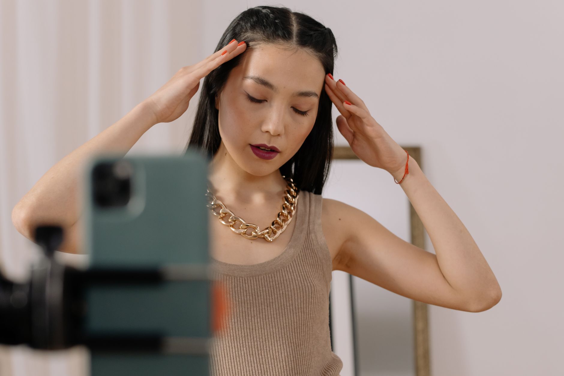 Woman poses gracefully with closed eyes, wearing a chain necklace and tank top indoors.