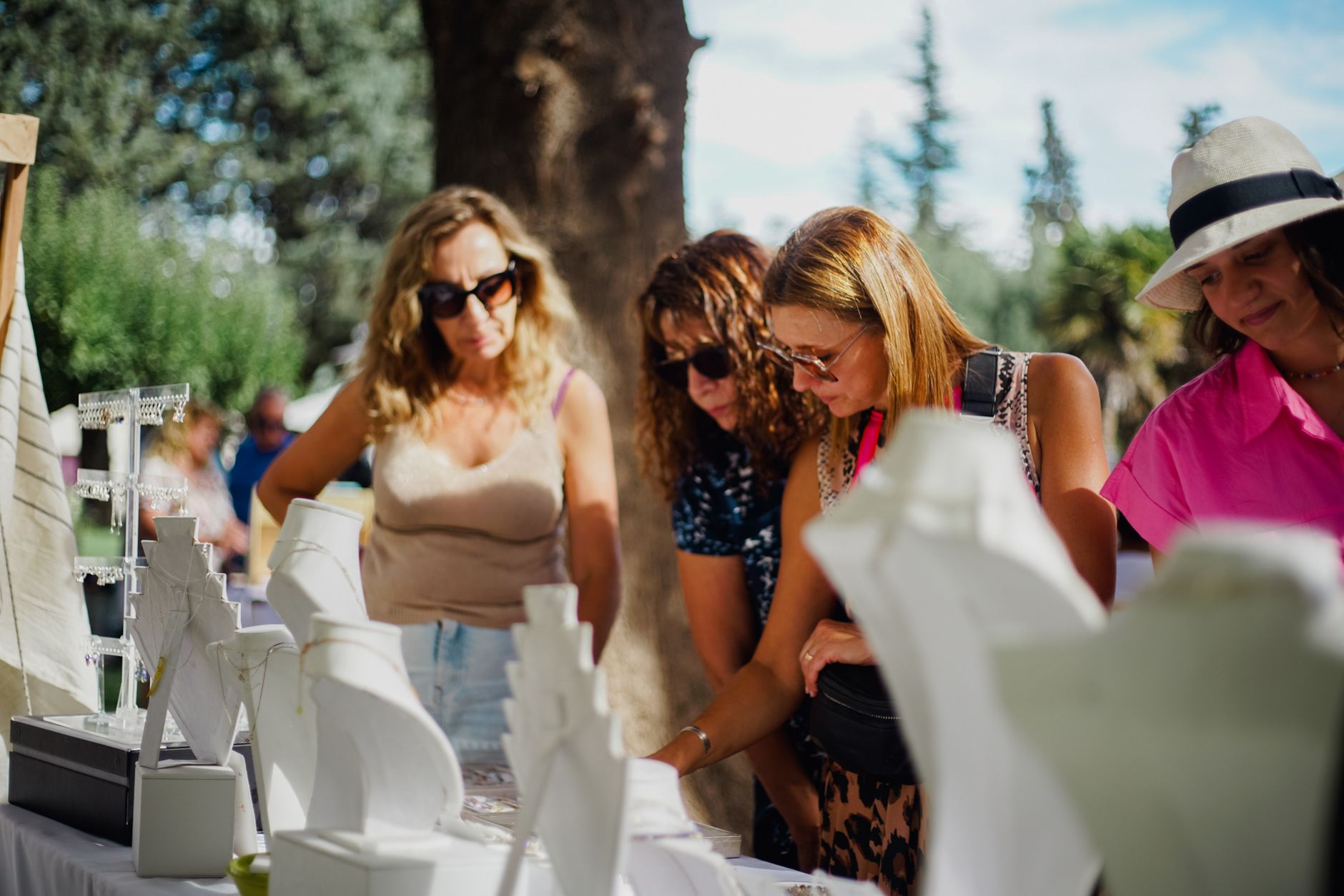 Group of women browsing jewelry at an outdoor market on a sunny day.