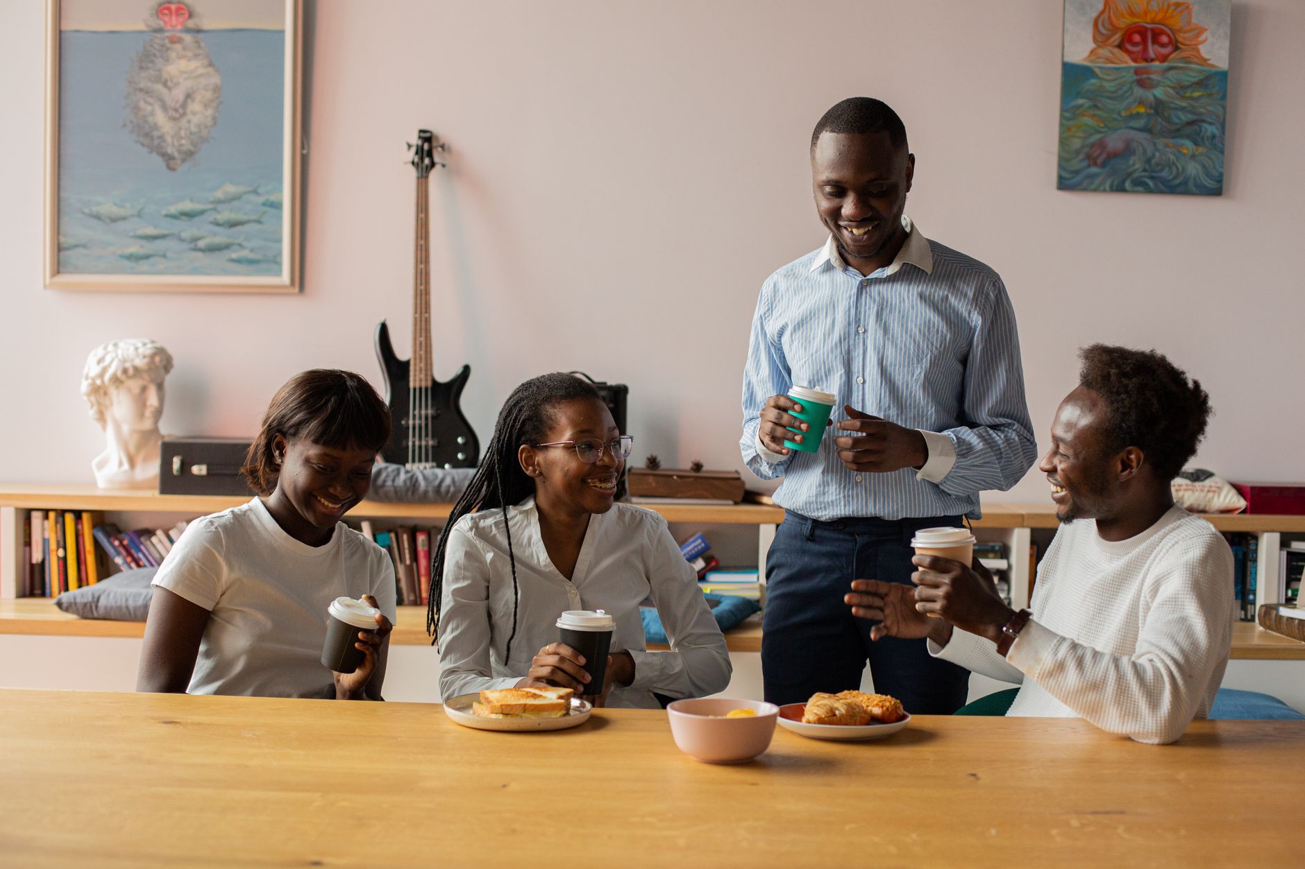 Group of colleagues having a coffee break in a modern office setting, sharing laughs and pastries.