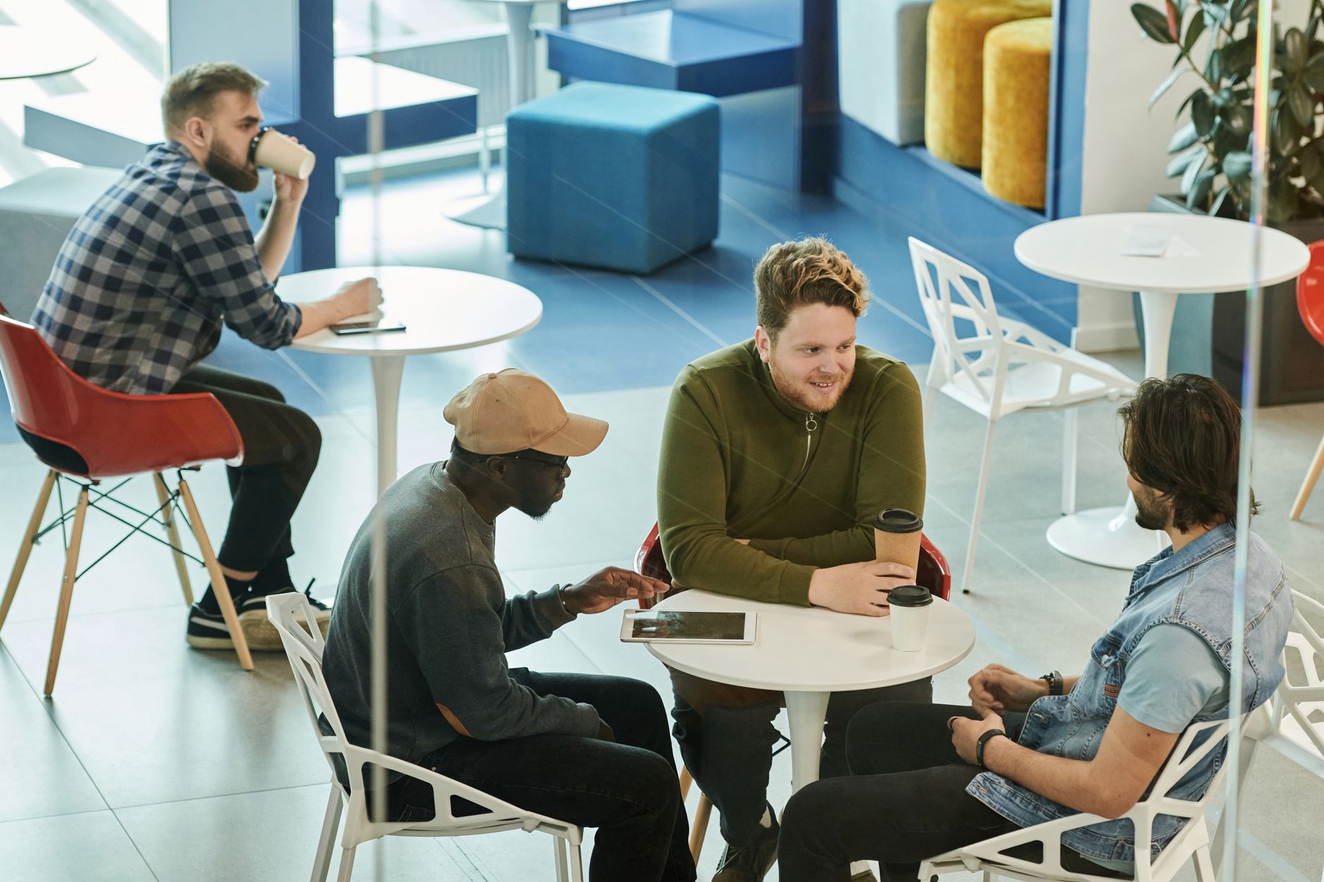 Diverse group of men enjoying coffee and conversation in a modern café setting.