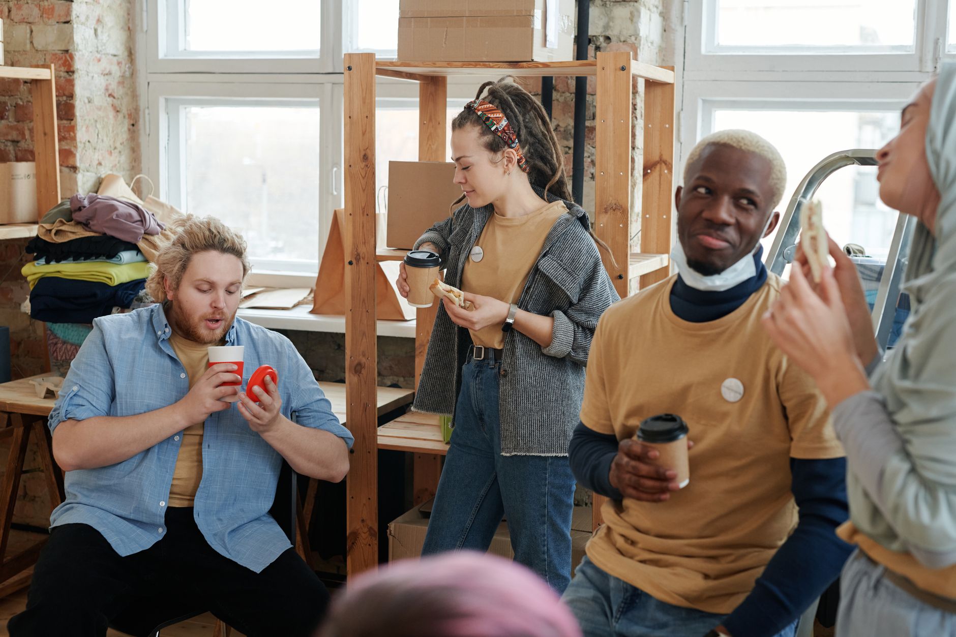A diverse group of volunteers taking a coffee break indoors, chatting and snacking together.