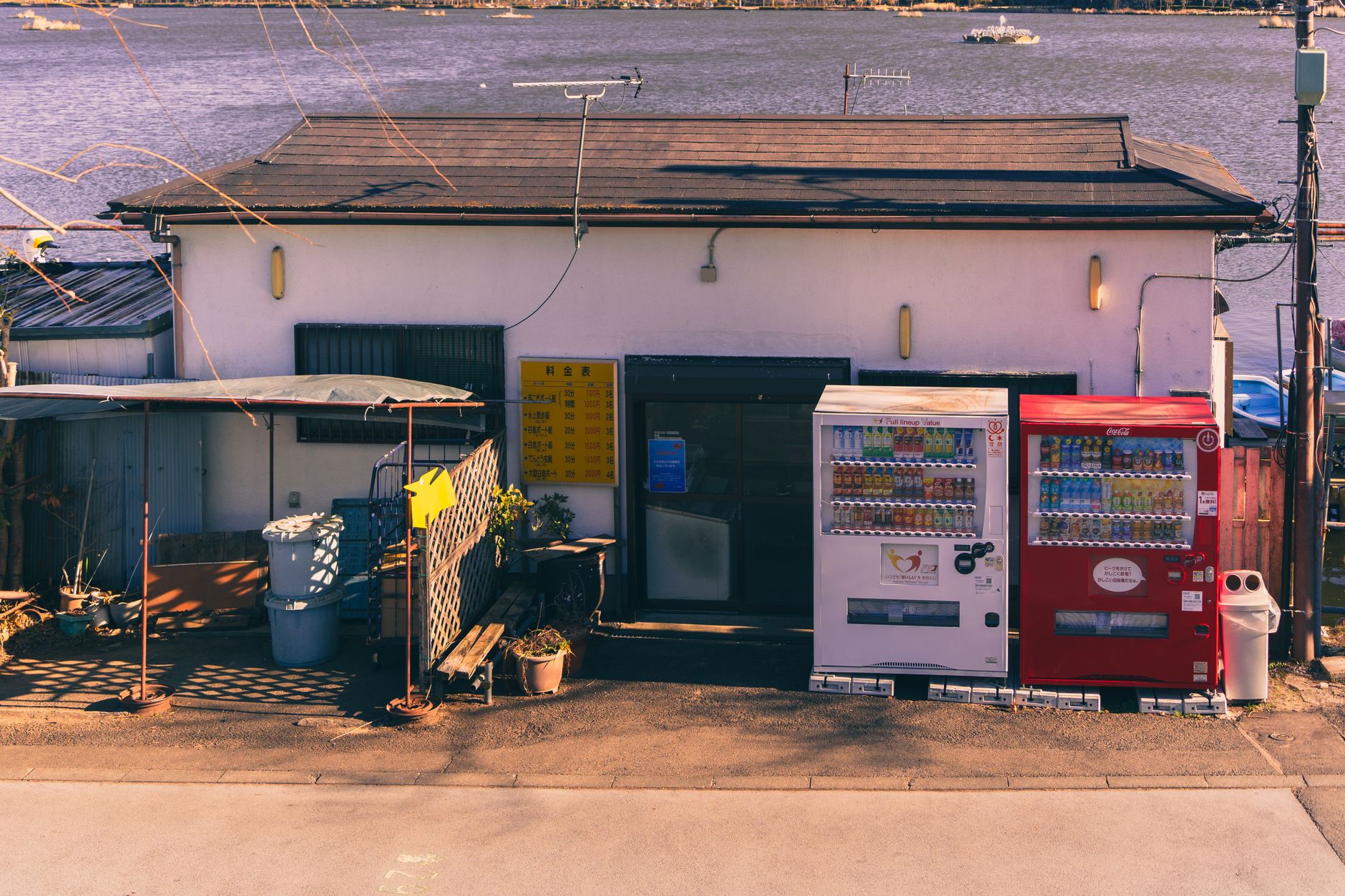 Japanese vending machines in front of a small shop by a tranquil lakeside during winter.