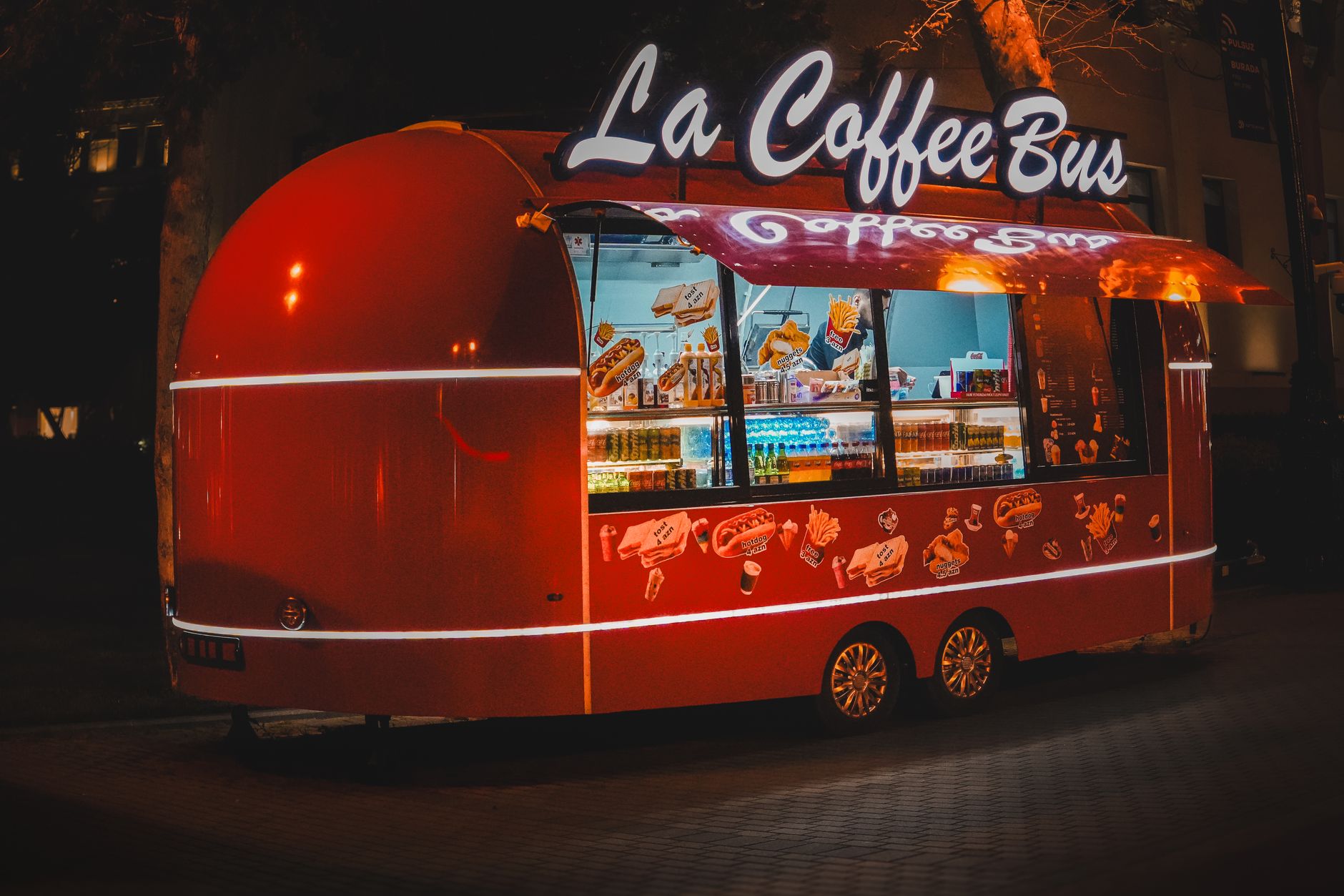 A colorful coffee bus serving food and drinks at night with eye-catching neon lights.