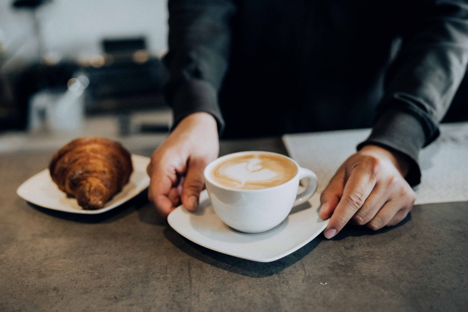 A barista places a latte and croissant on a counter, creating a warm cafe atmosphere.