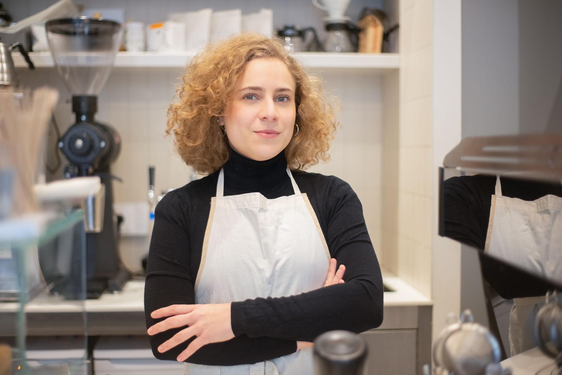 Confident barista standing in a modern café surrounded by coffee equipment.