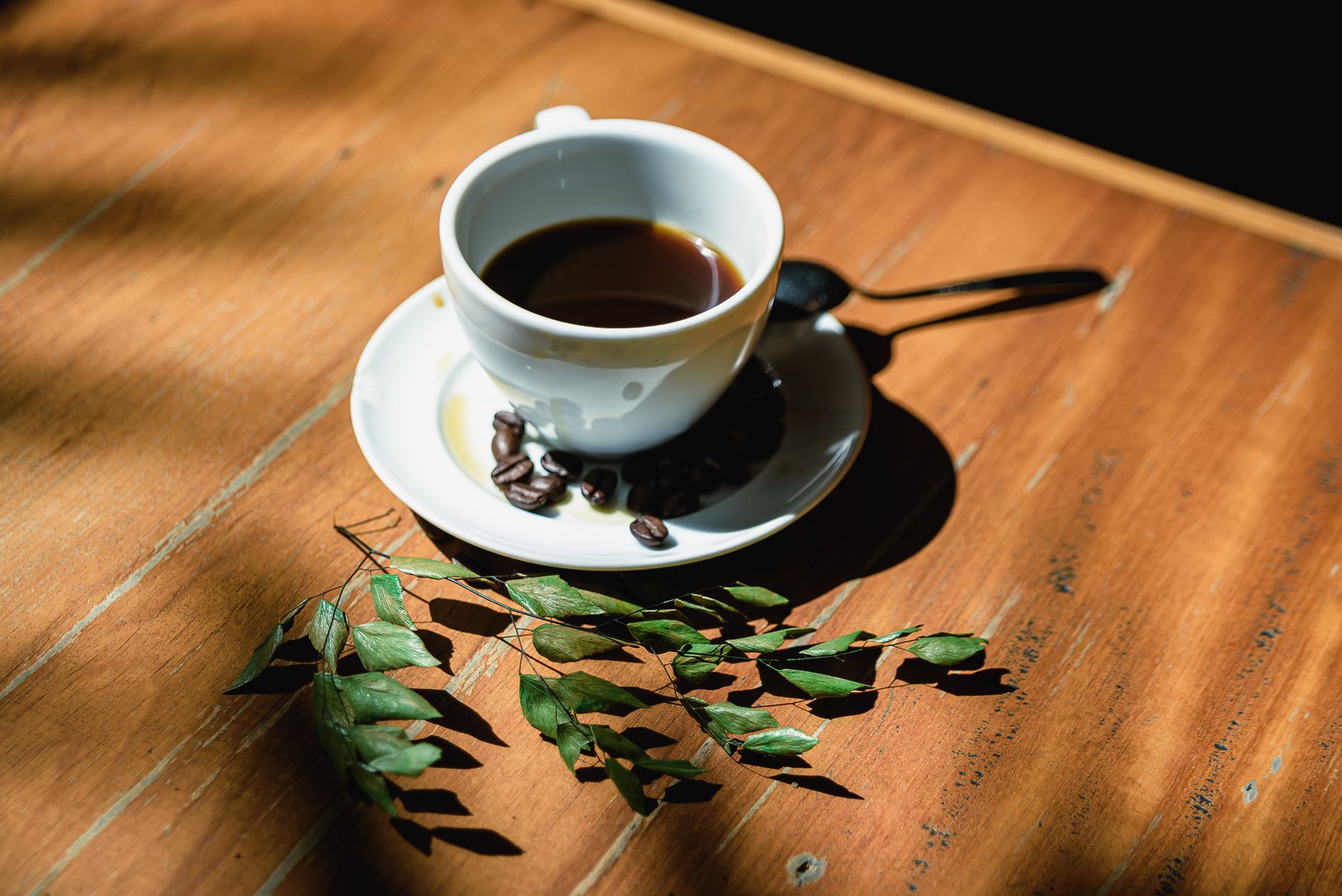 Wooden table with coffee cup, beans, and leaves creating a warm still life.
