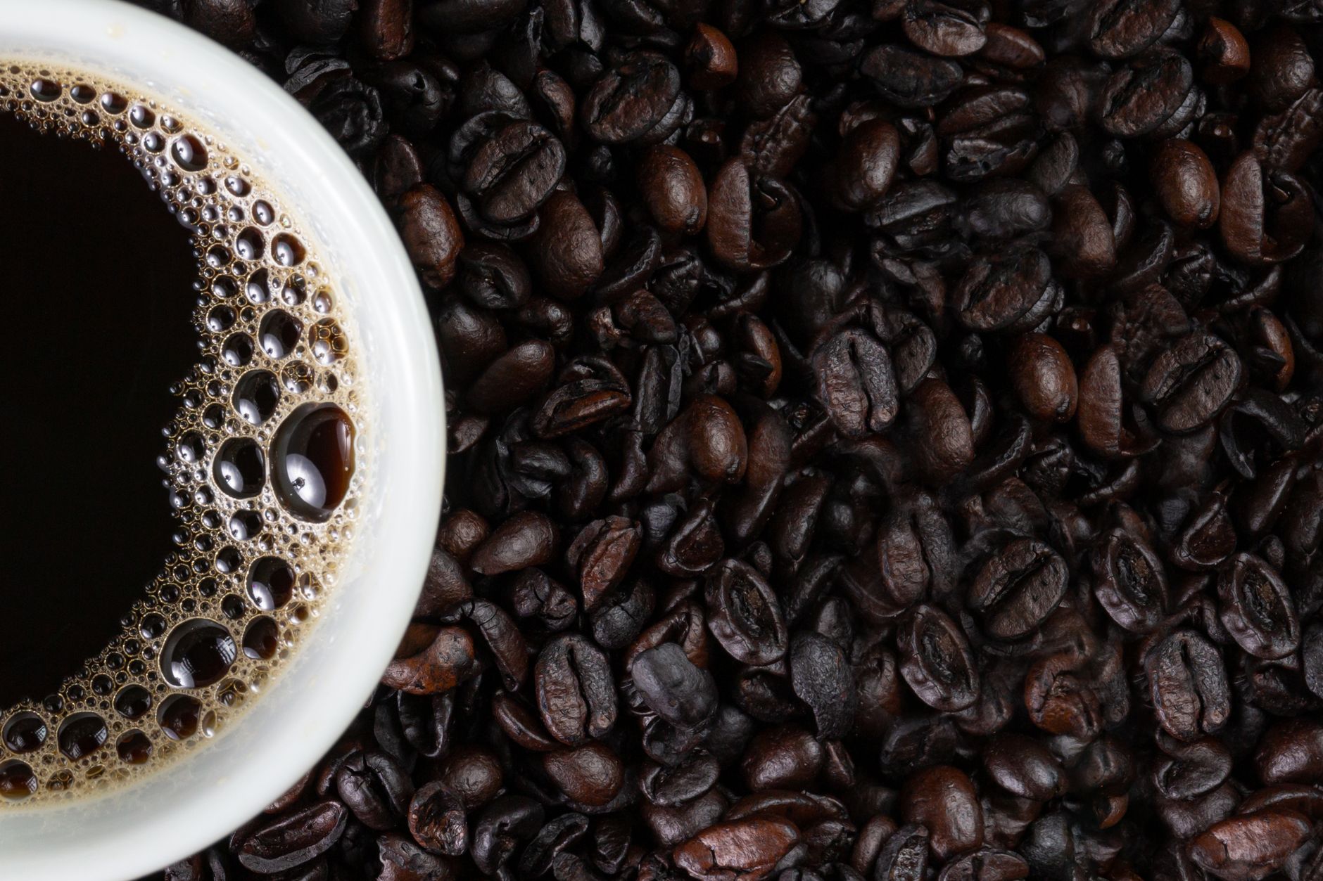 A close-up of a cup of coffee surrounded by roasted coffee beans in a flat lay composition.