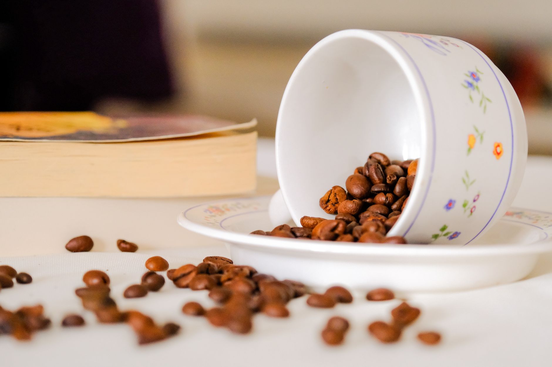 A floral coffee cup tipped over spilling coffee beans on a table, adding a rustic charm.