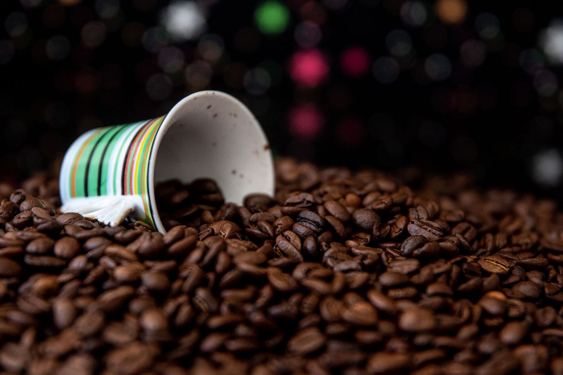 Close-up of a tipped mug spilling coffee beans against a bokeh background.