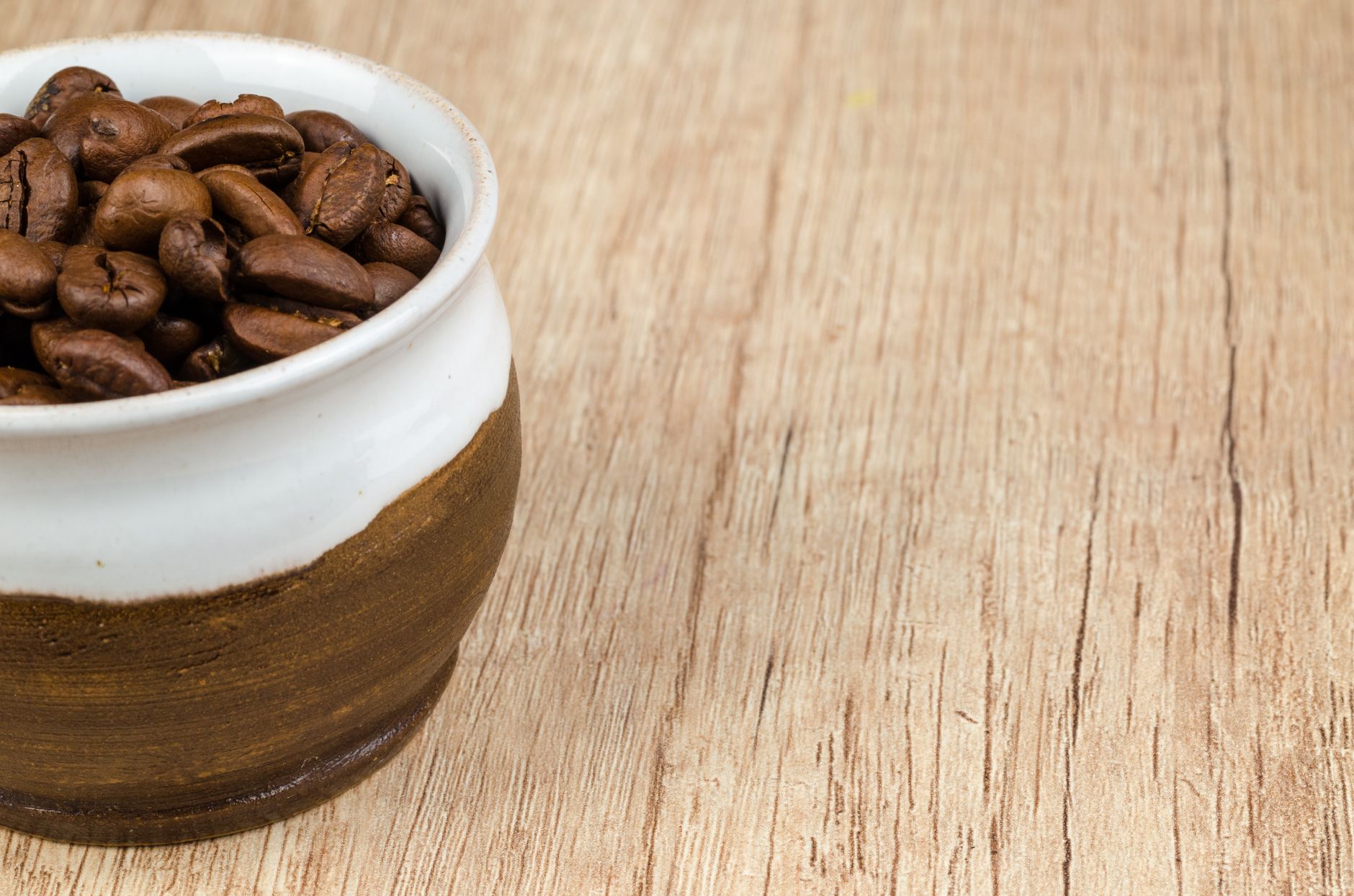 Close-up view of aromatic coffee beans in a rustic ceramic cup on wooden table.