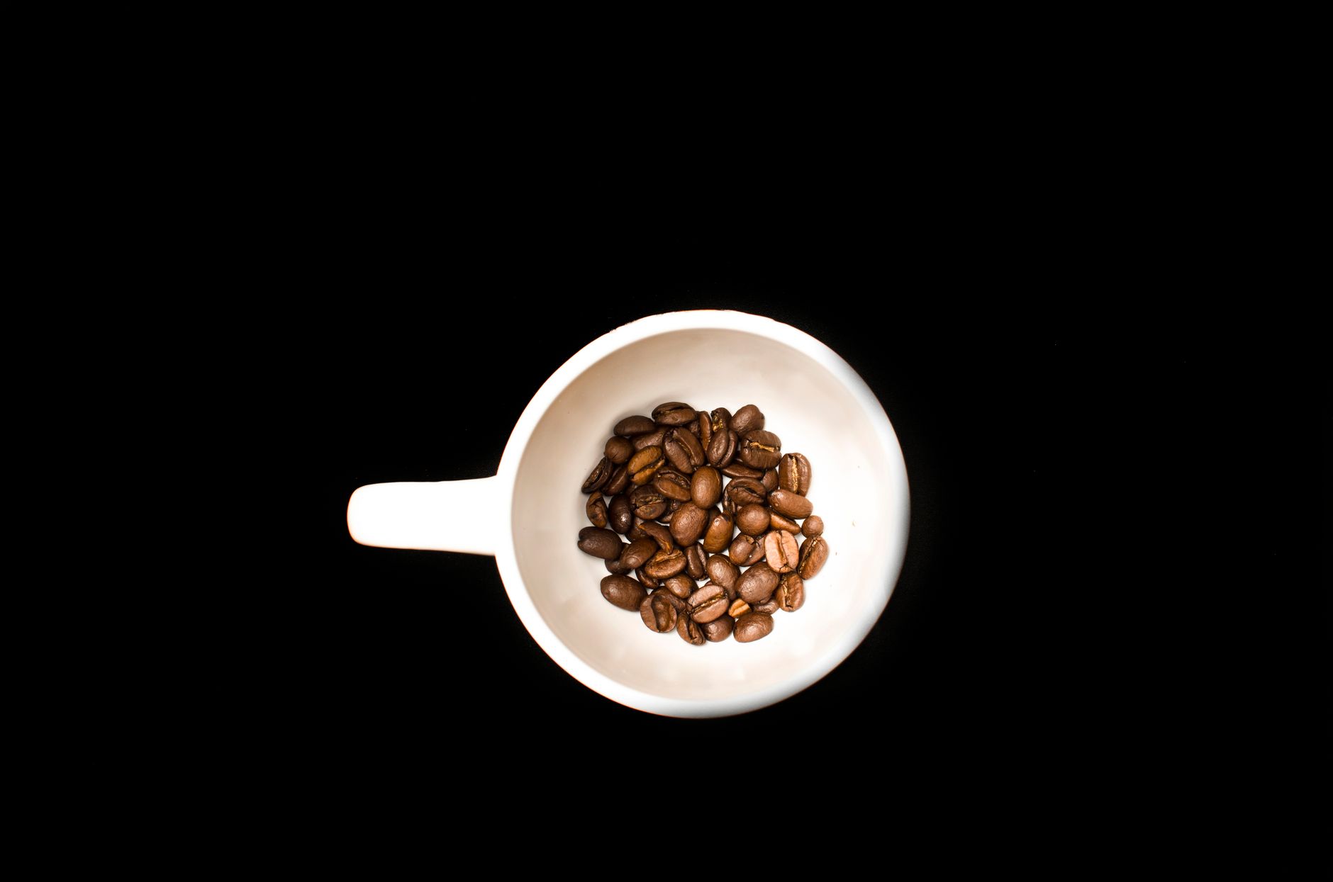 Coffee beans in a white cup against a black background, minimalist style.