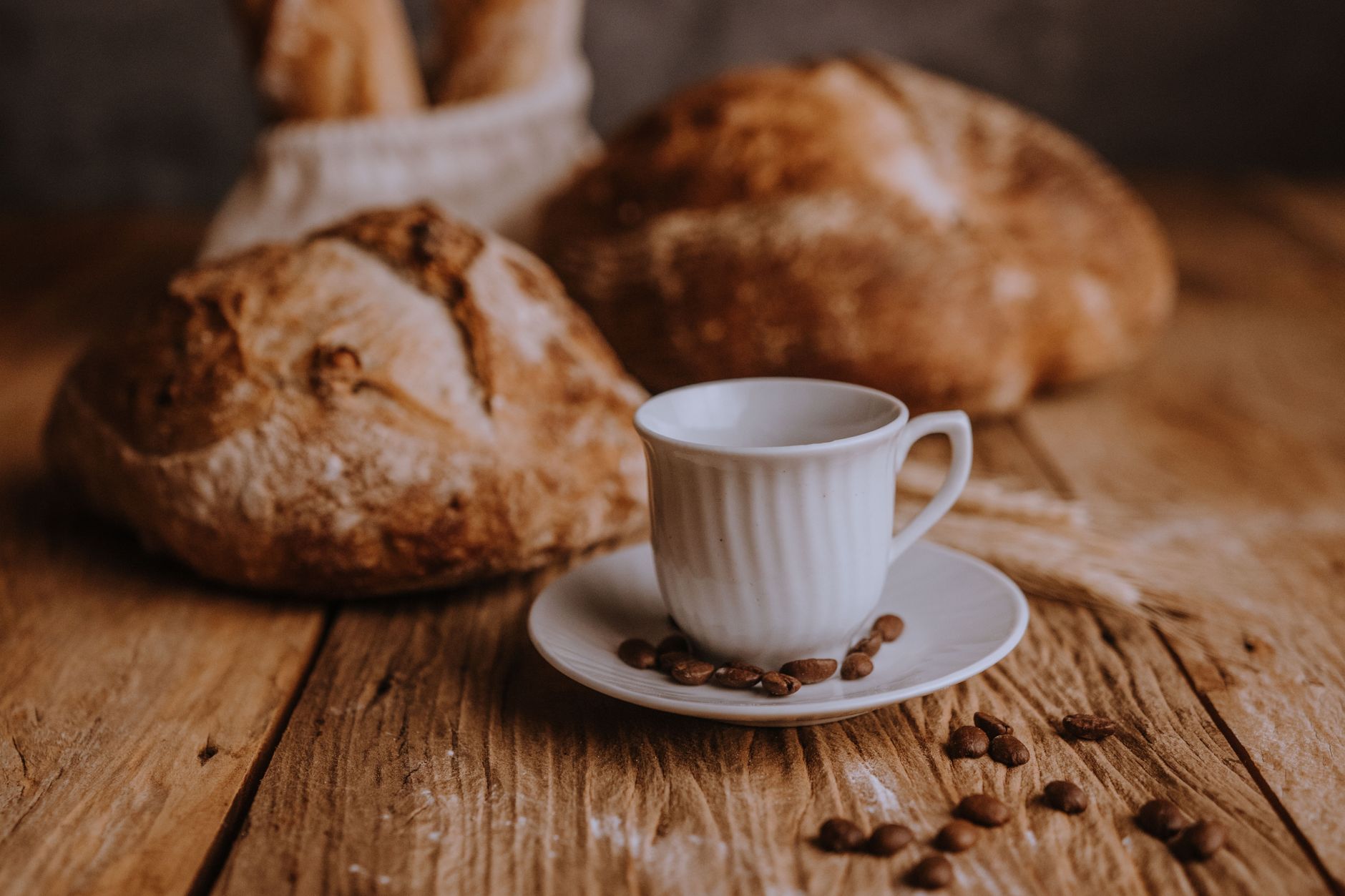 Artistic arrangement of fresh bread and a coffee cup on a rustic wooden table with scattered coffee beans.