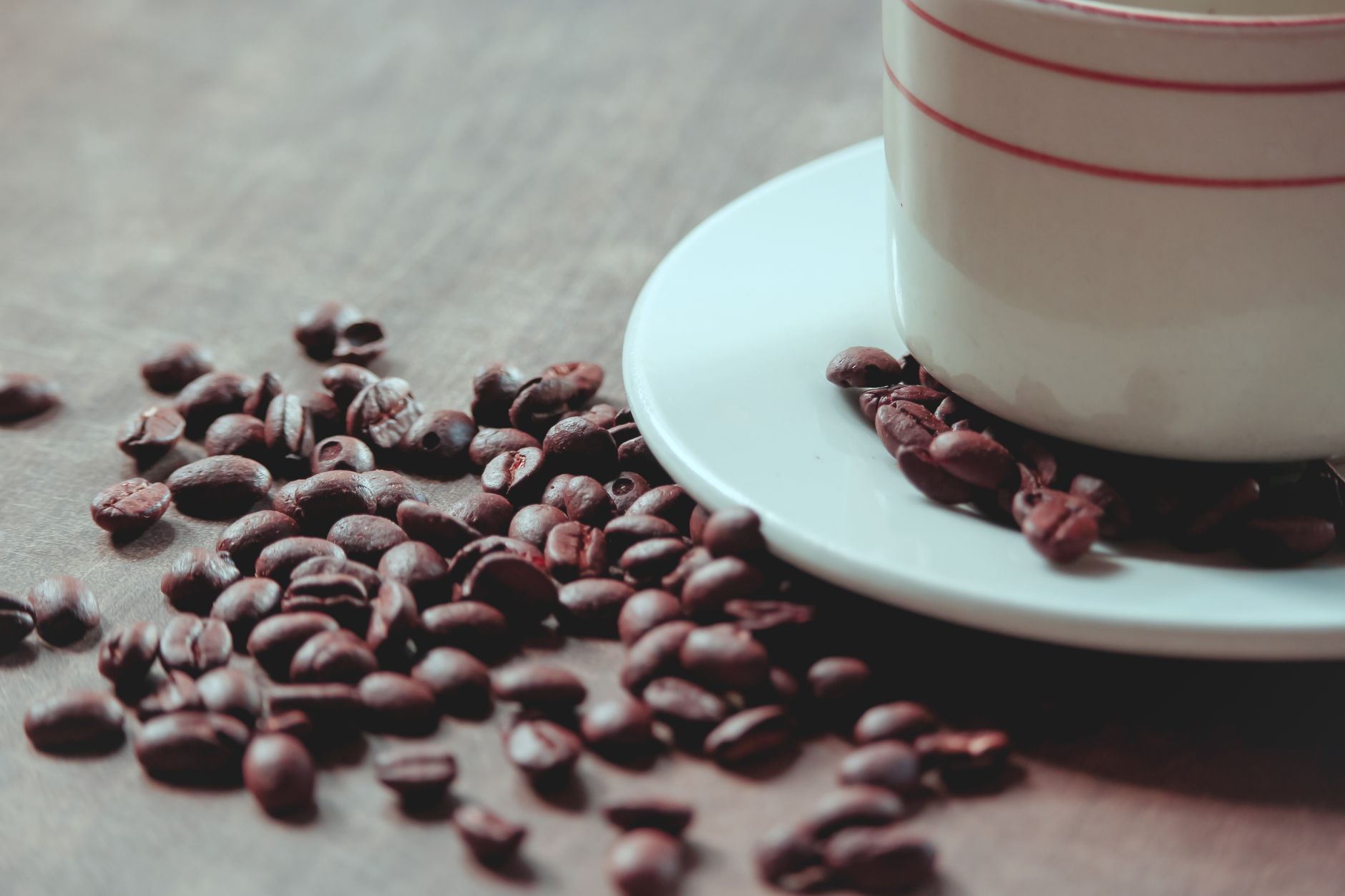A close-up of roasted coffee beans next to a cup and saucer on a wooden surface.