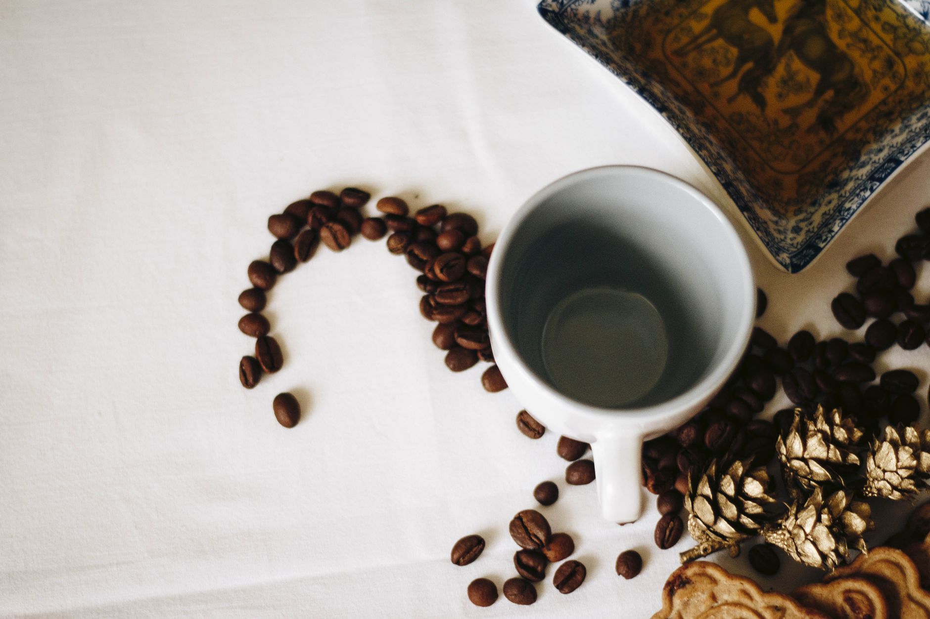 Creative top-down view of coffee beans forming a pattern with an empty cup and decorative elements.