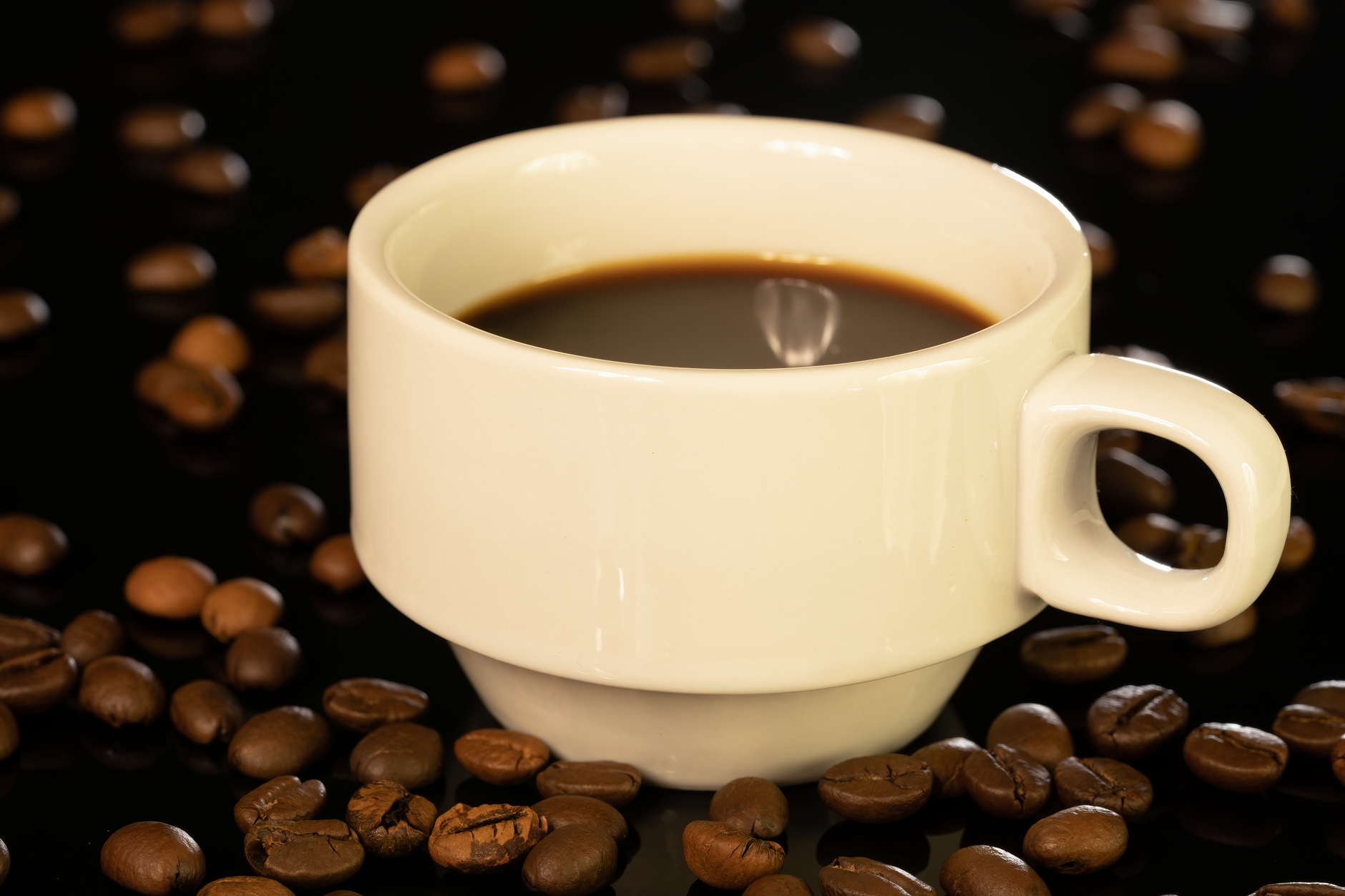A classic white cup of black coffee surrounded by coffee beans on a dark background.