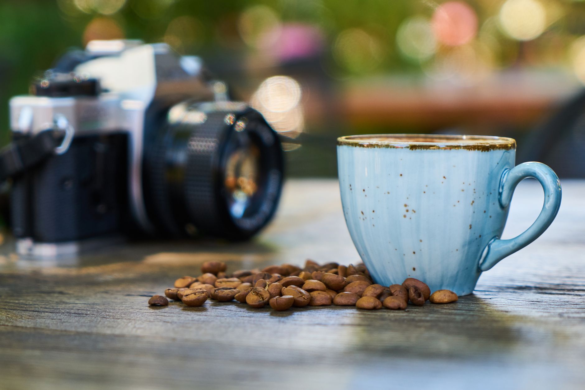 Close-up shot of a coffee cup, beans, and camera on a wooden table.
