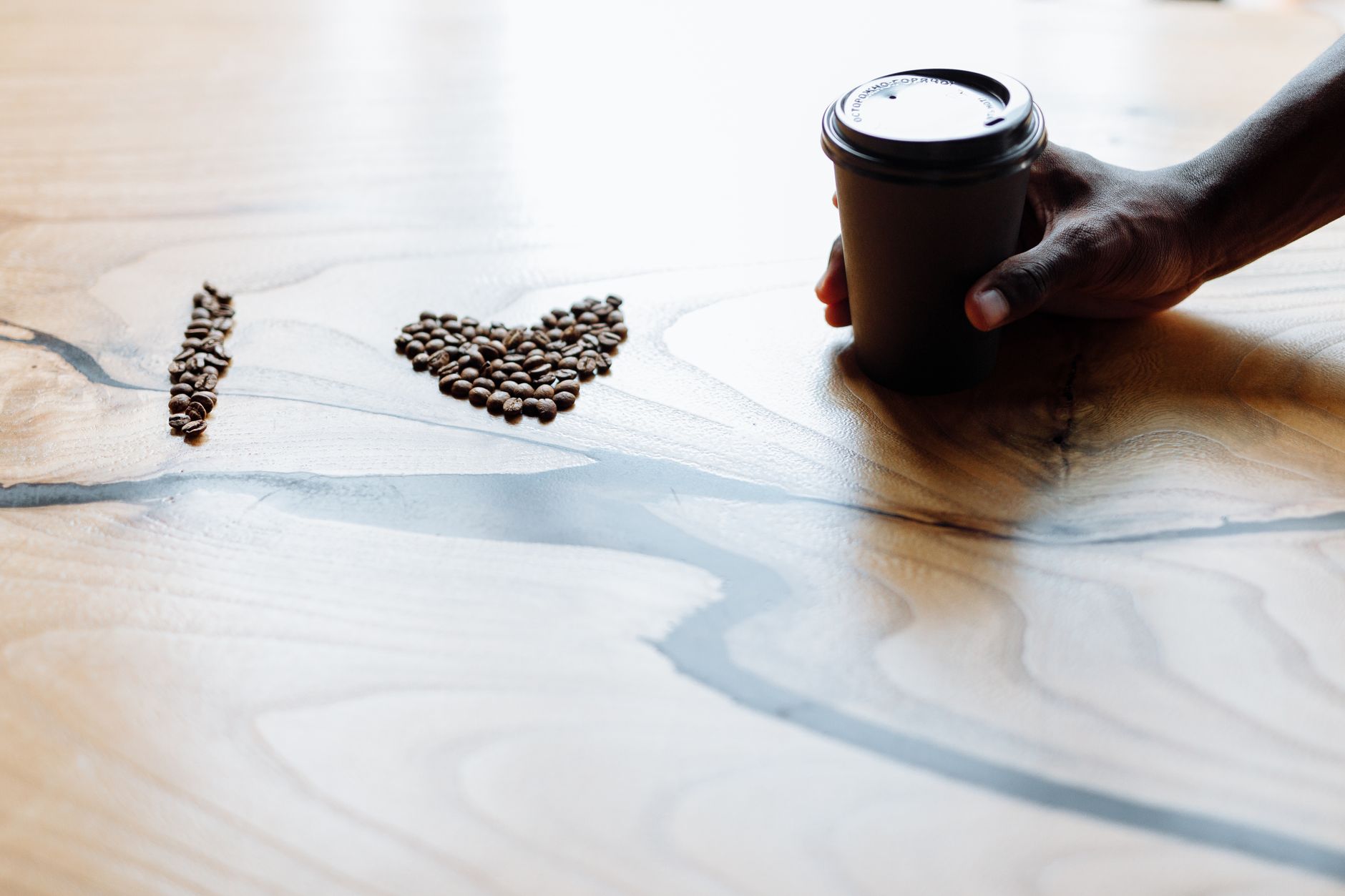 Coffee beans forming love shape on wooden table with hand holding a cup creating a warm, inviting scene.
