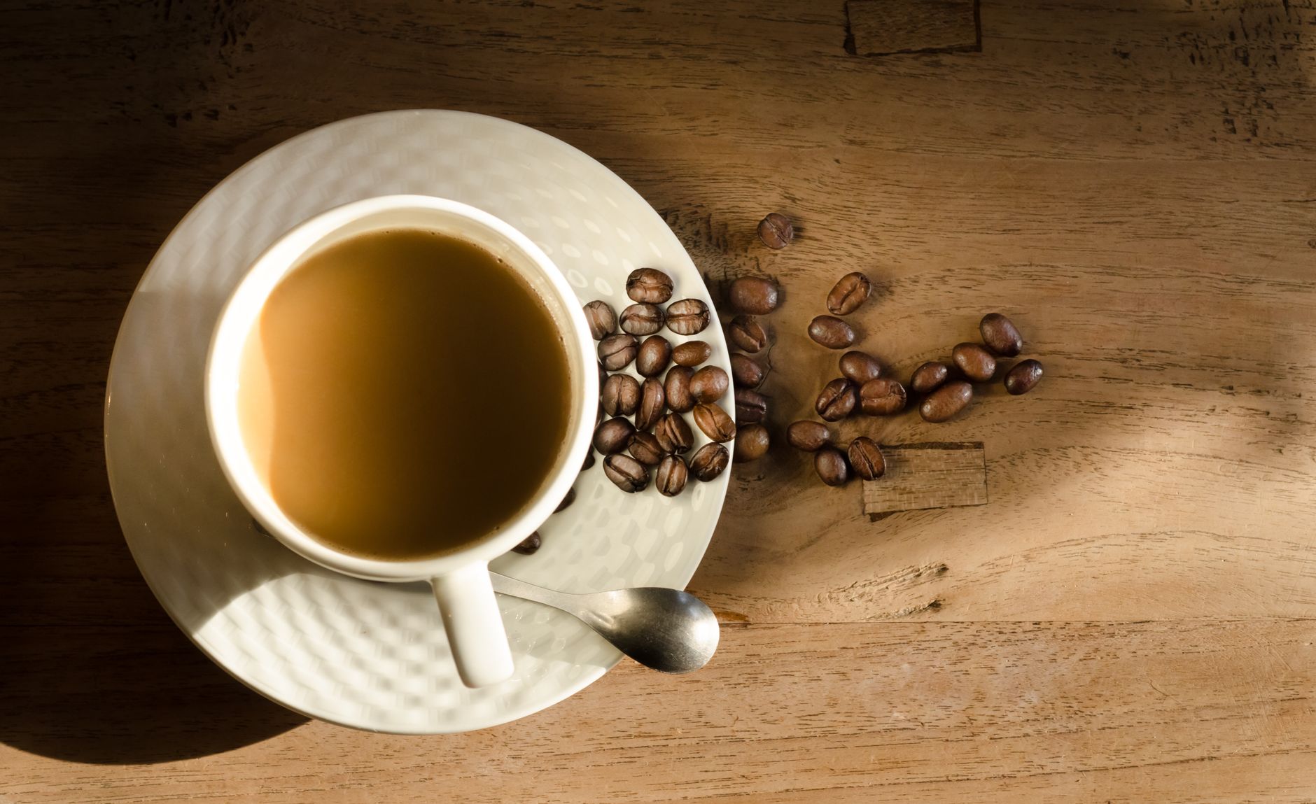 Top view of a cup of coffee on a wooden table with scattered beans.