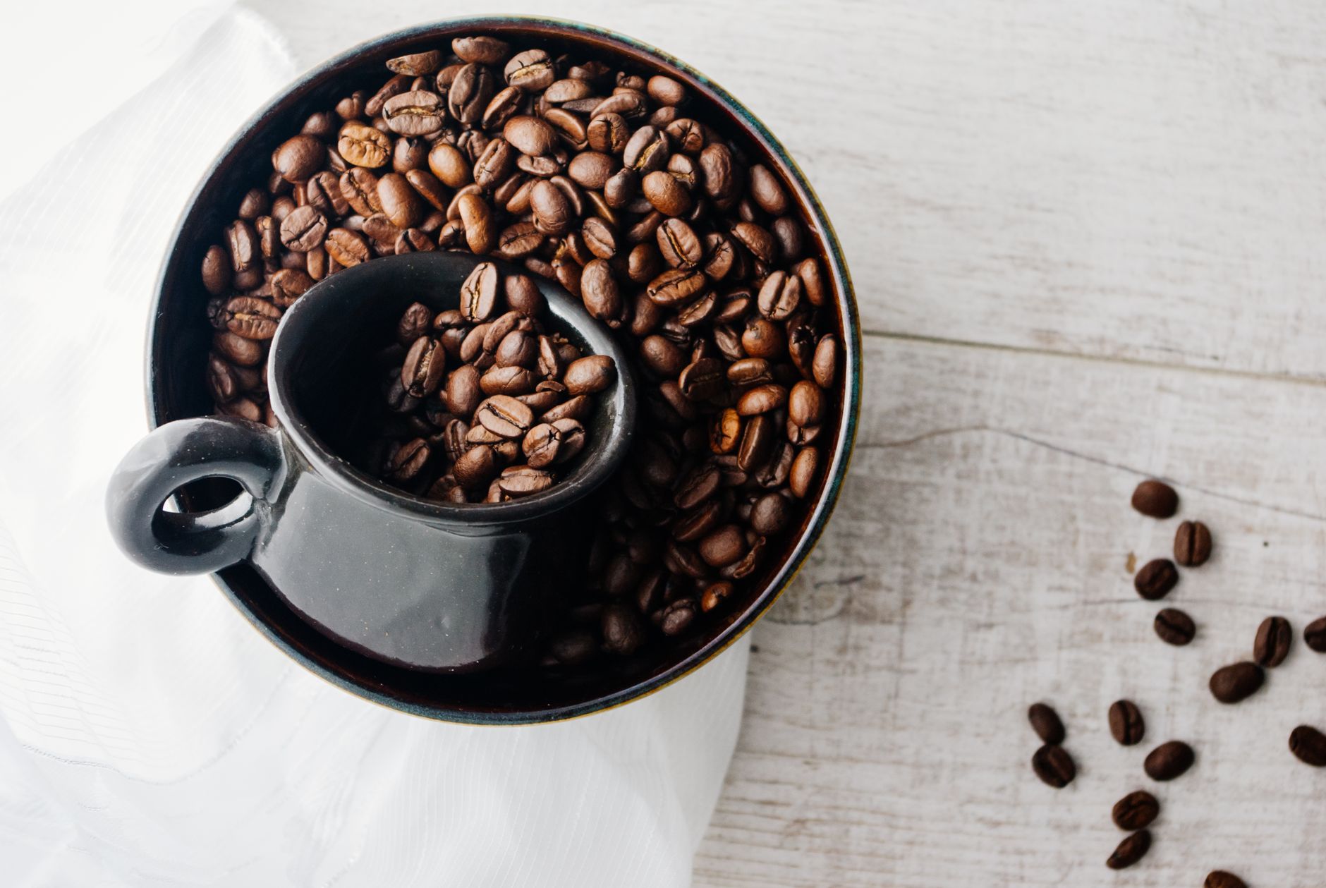 From above of ceramic cup placed in bowl with coffee beans against wooden background in daytime