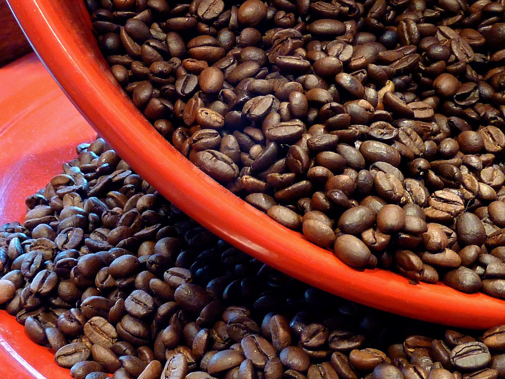 Close-up of roasted coffee beans spilling from a red bowl, showcasing rich textures and vibrant colors.