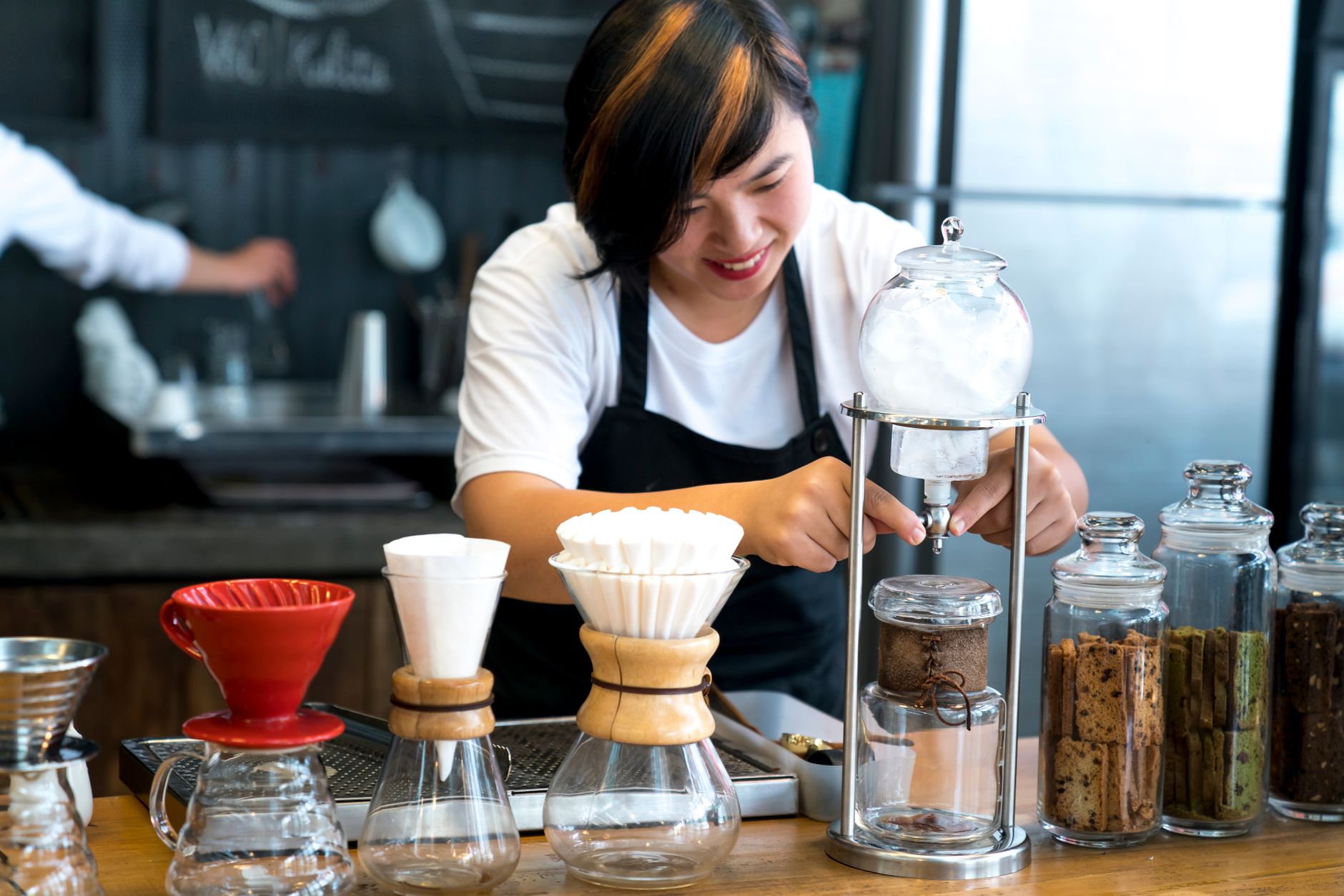 Smiling barista making coffee using various equipment in a modern café setting.