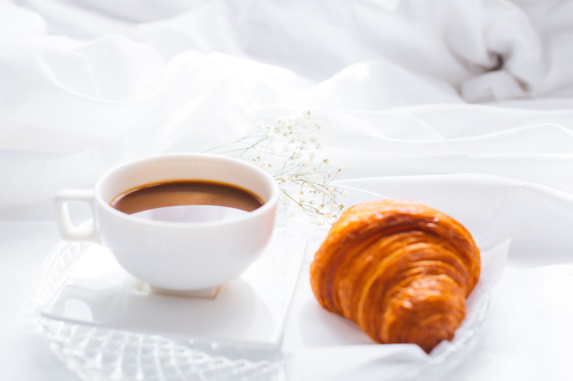 A serene breakfast setting with coffee and a croissant on white linens, perfect for a relaxing morning.