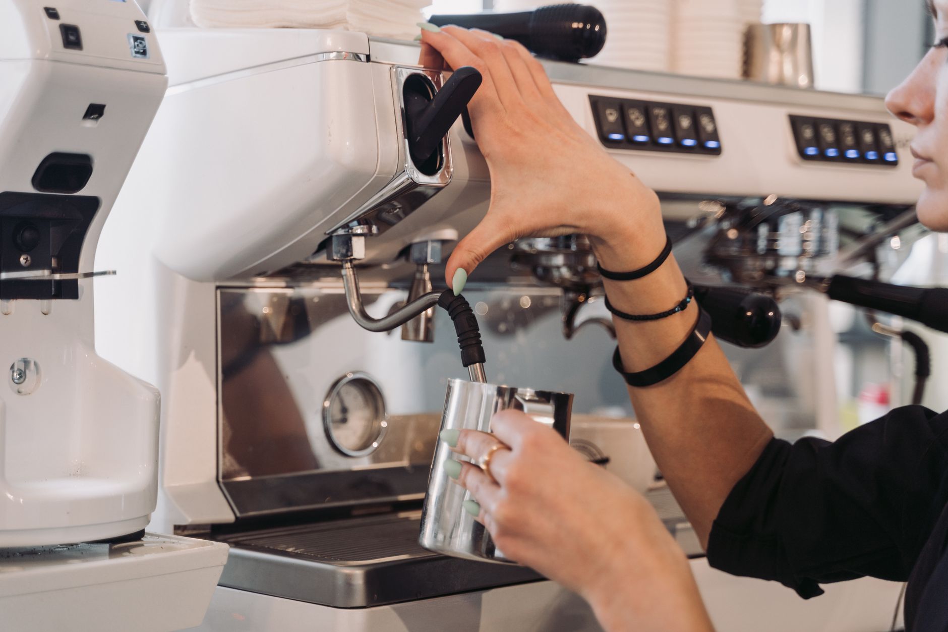 Close-up of barista steaming milk at a modern espresso machine indoors.