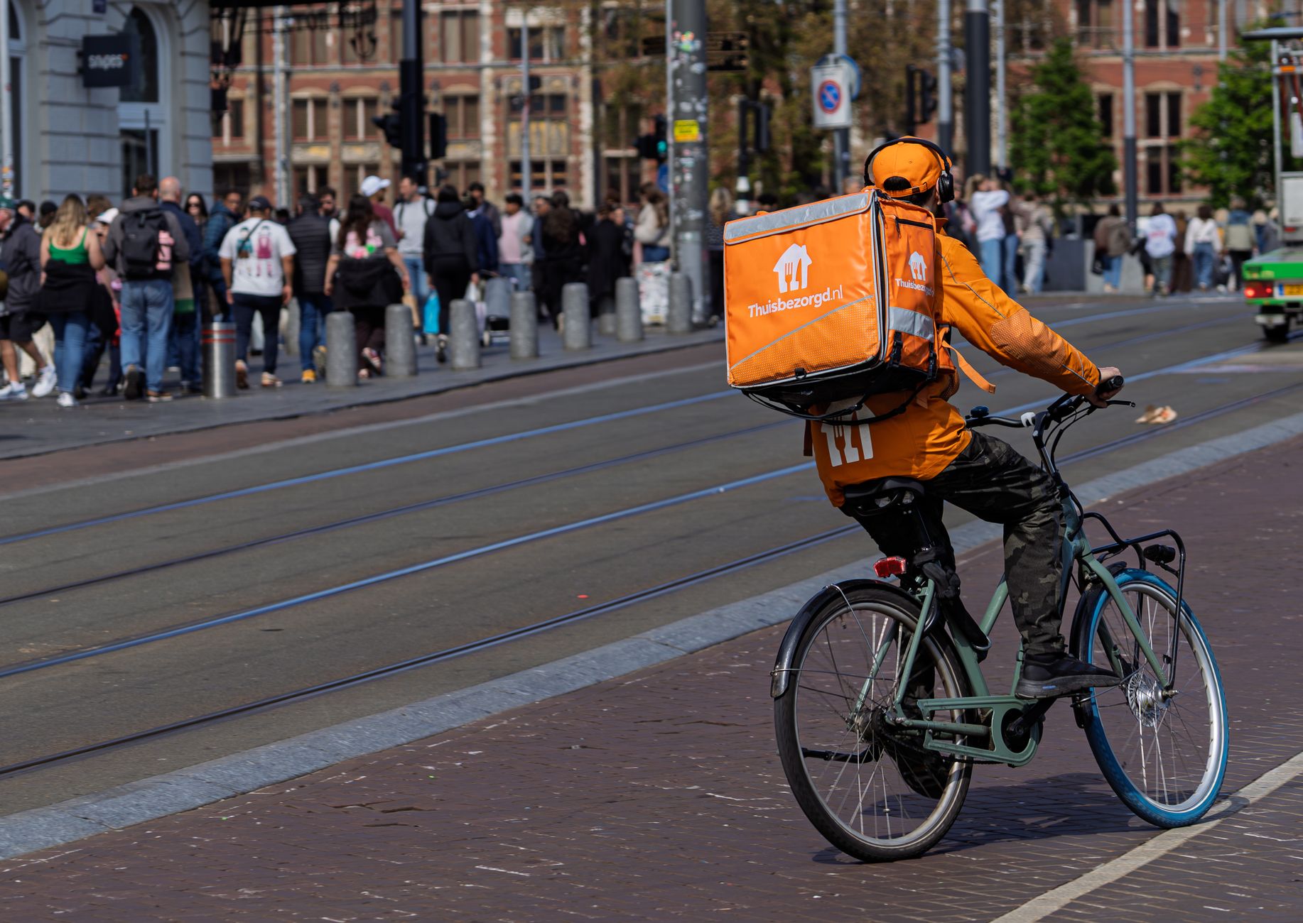 Cyclist with delivery backpack rides through busy city street on a sunny day.