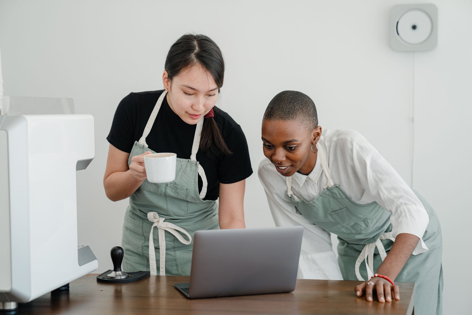Young Asian coffee house worker explaining to new African American coworker how to use special computer program during break at work