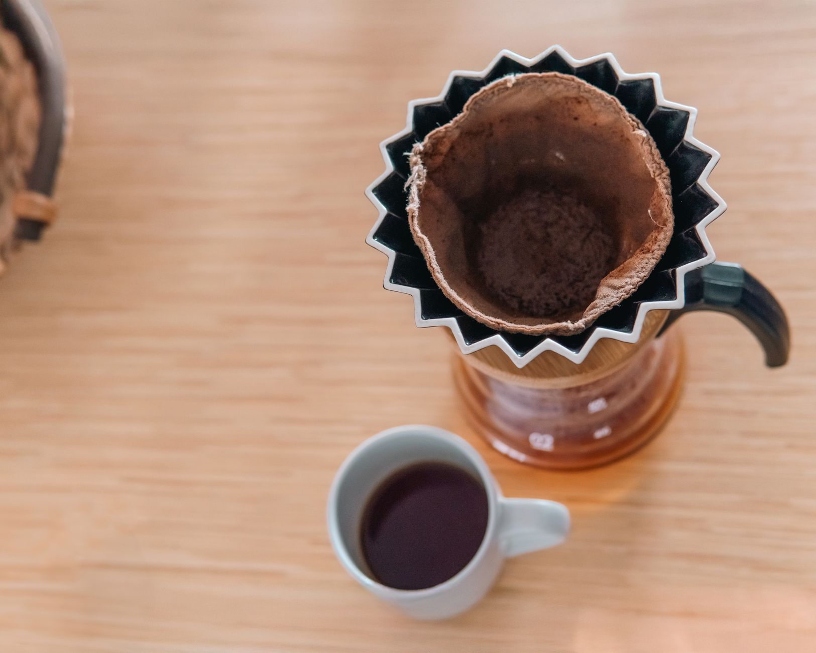 Top view of coffee pot with cloth filter and cup on wooden table.