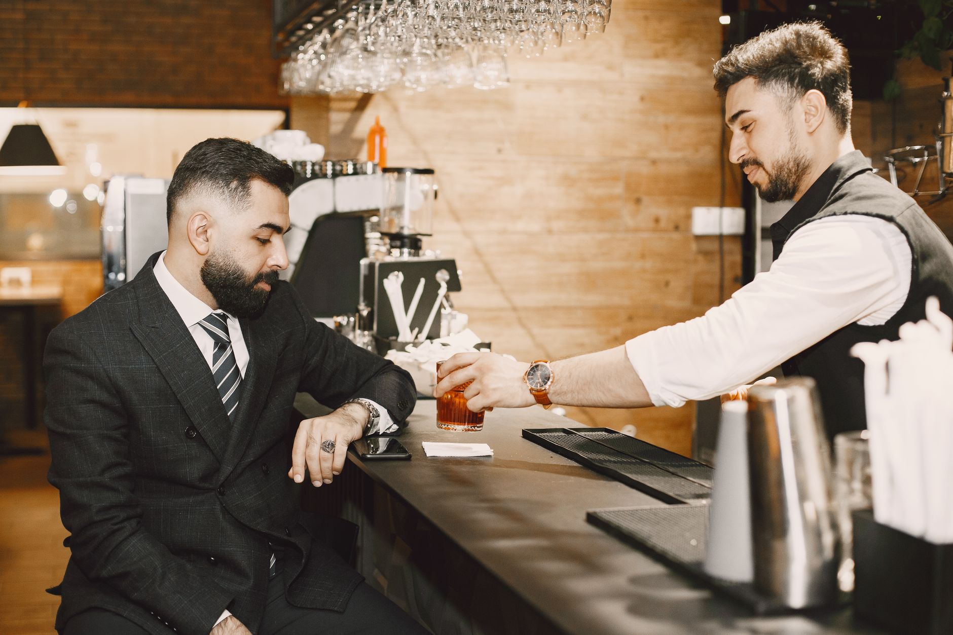 A bartender serves a drink to a business client at a stylish bar counter.