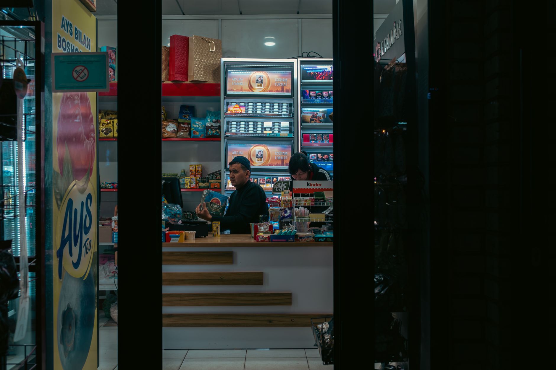 Interior of a convenience store in Uzbekistan with two adults manning the counter at night.