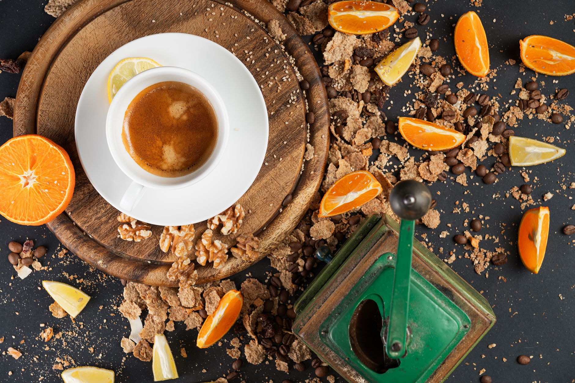 A flat lay of coffee, citrus fruits, nuts, and a vintage grinder on a wooden board.