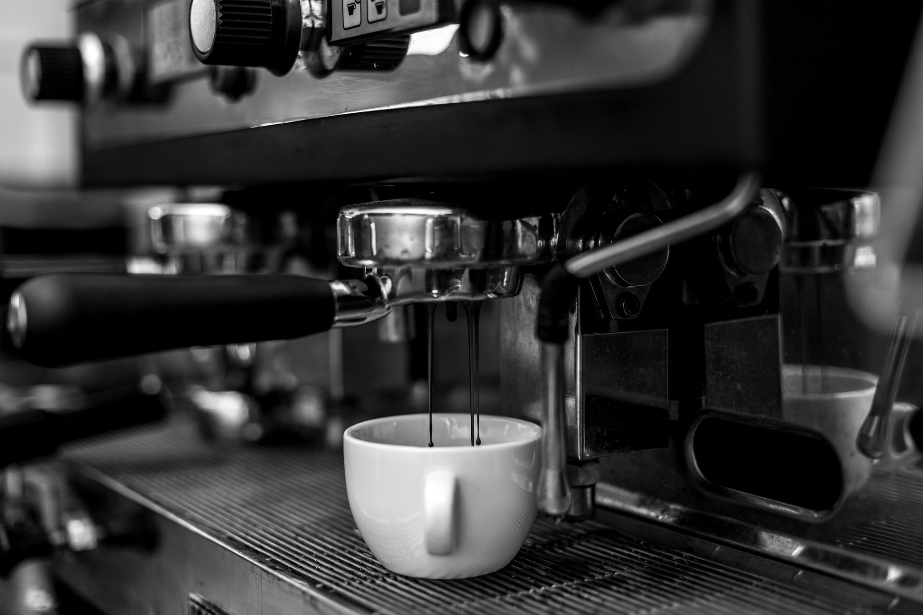 Monochrome close-up of an espresso machine pouring coffee into a cup.