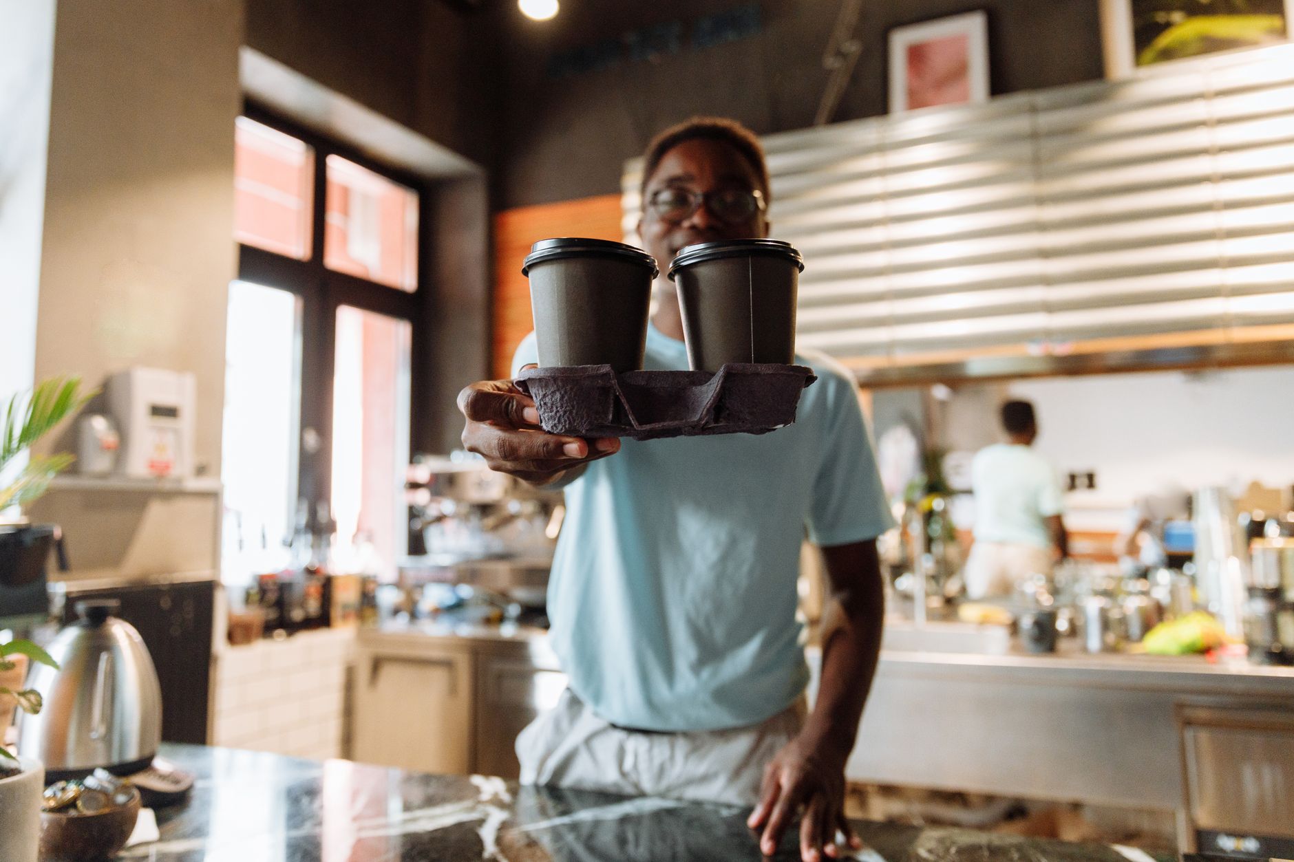 A friendly barista handing two takeaway coffee cups inside a cozy cafe setting.
