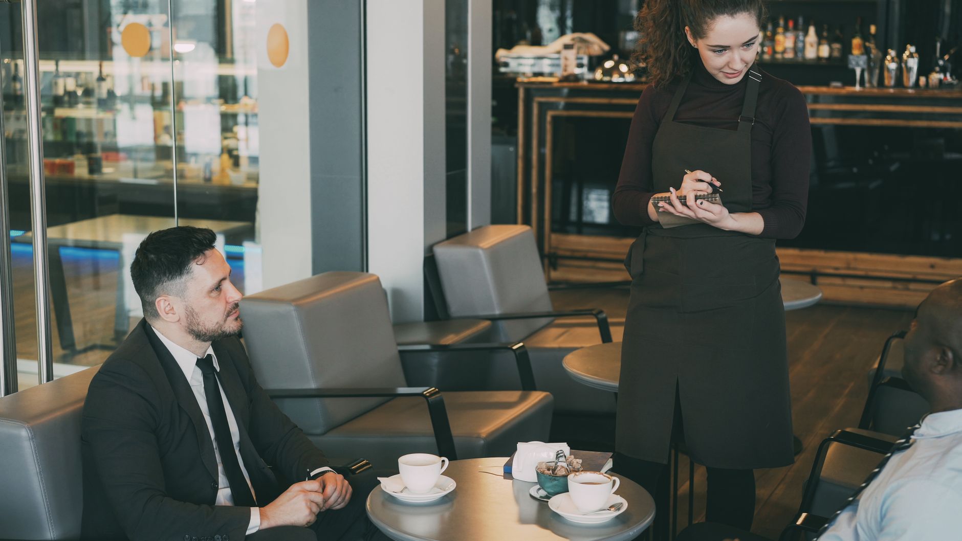 Casual business meeting at a modern café with two professionals and a waiter.