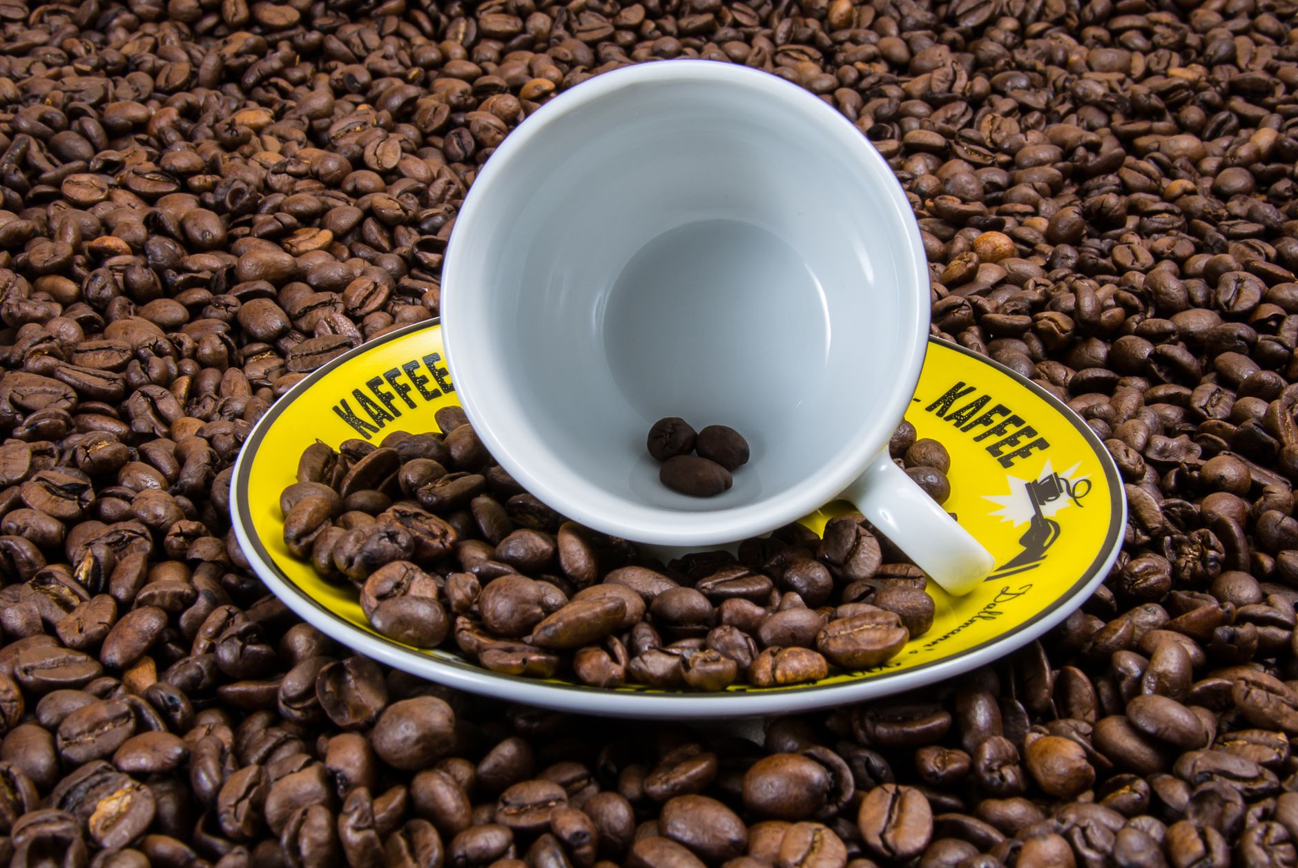 An empty coffee cup on a yellow saucer surrounded by roasted coffee beans.