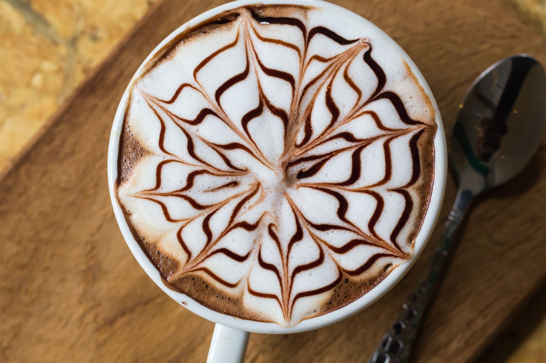 Close-up of a cappuccino with intricate chocolate pattern on foam, served on a wooden table.