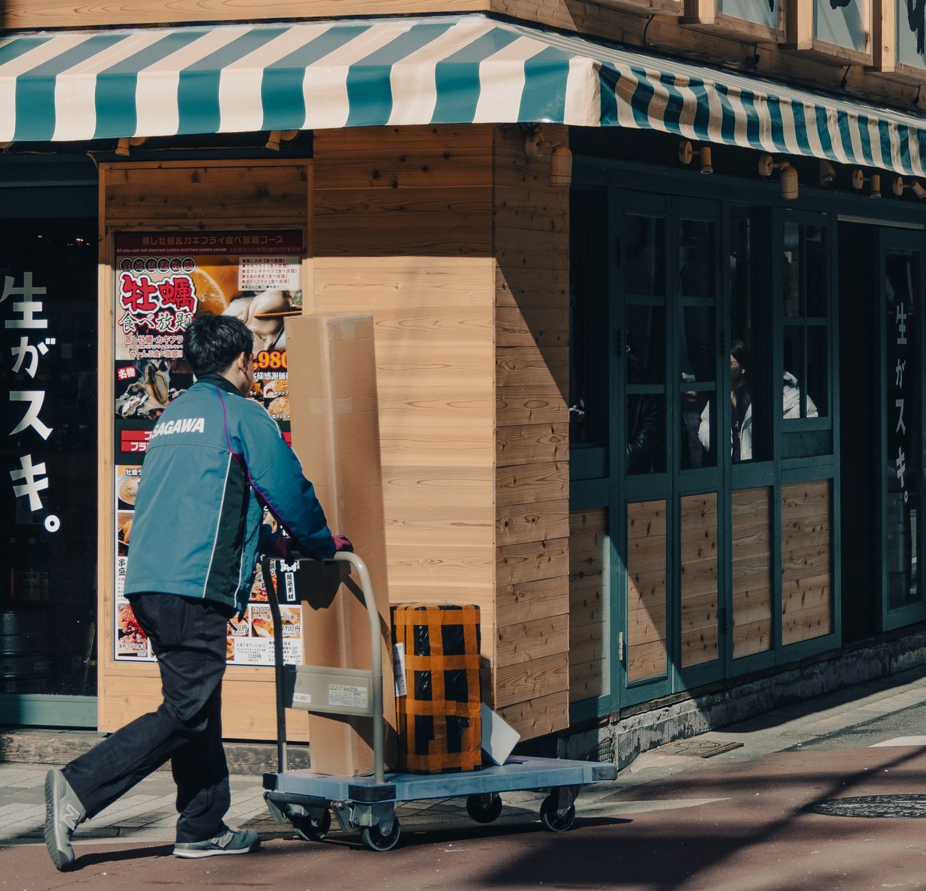 A courier pushes a cart with packages outside a wooden storefront on a sunny day.