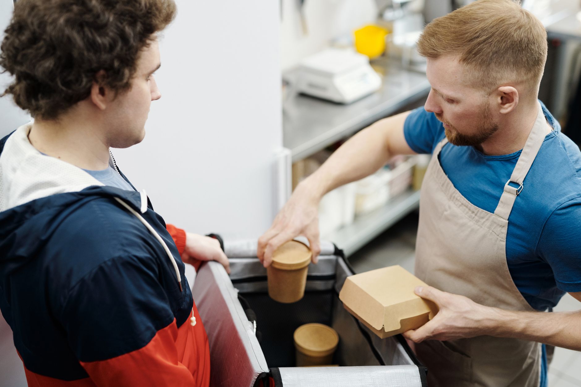 Delivery worker in apron packing food in container for customer. Indoor setting.
