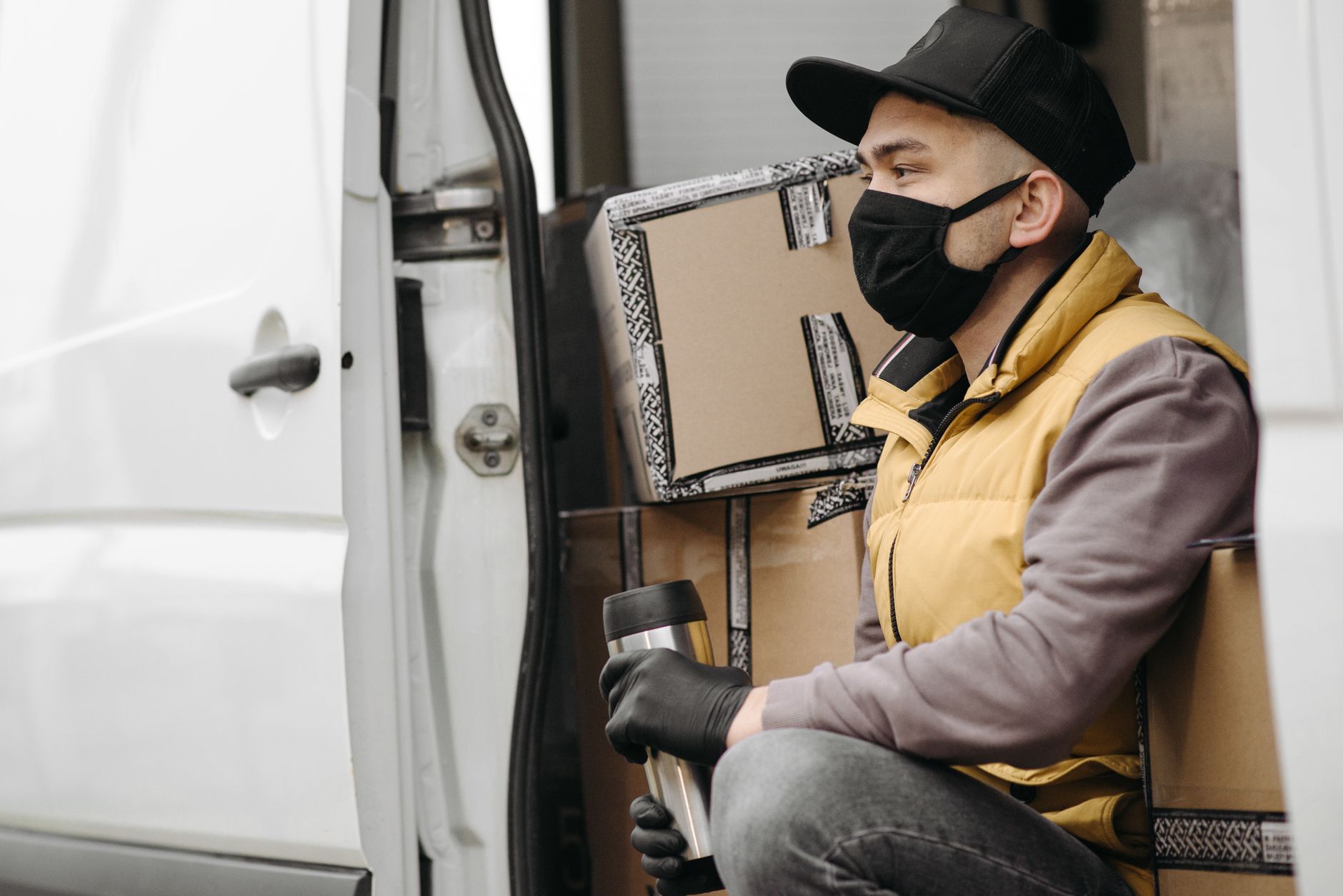 A courier wearing a face mask is seated in a van surrounded by packages, representing modern delivery services.