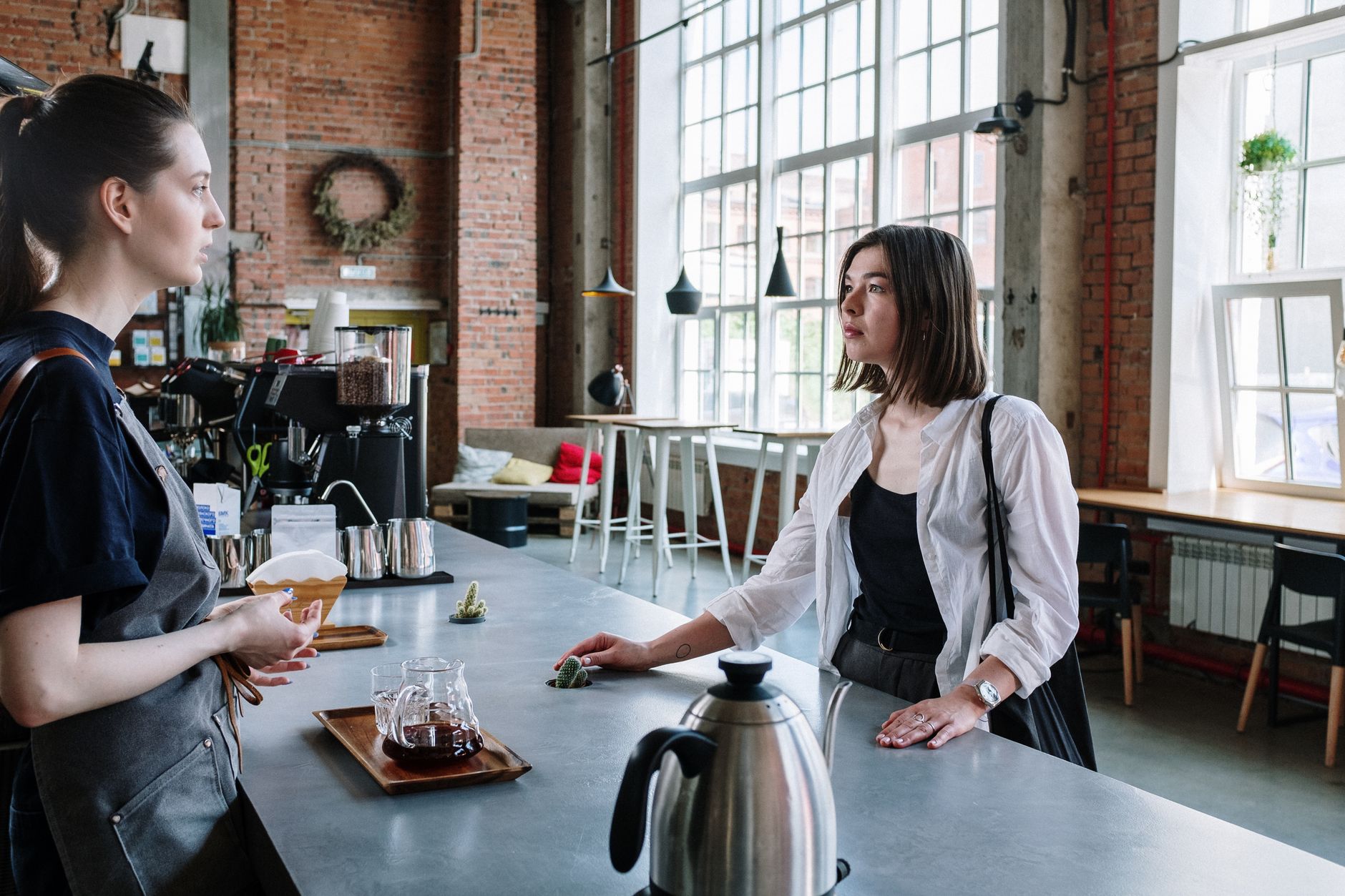 A barista and customer engage in a conversation at a stylish café counter with exposed brick walls.