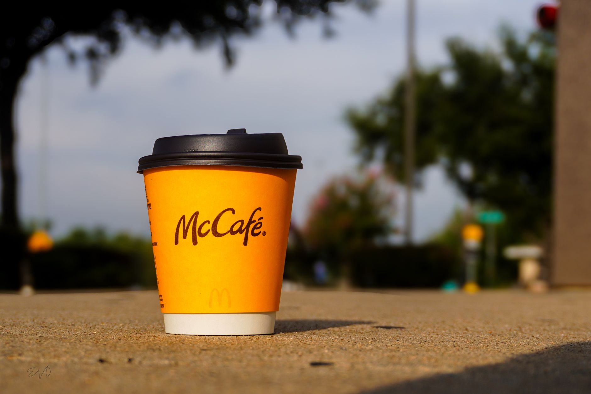 McCafé cup on concrete surface in Houston, Texas with blurred trees in background.