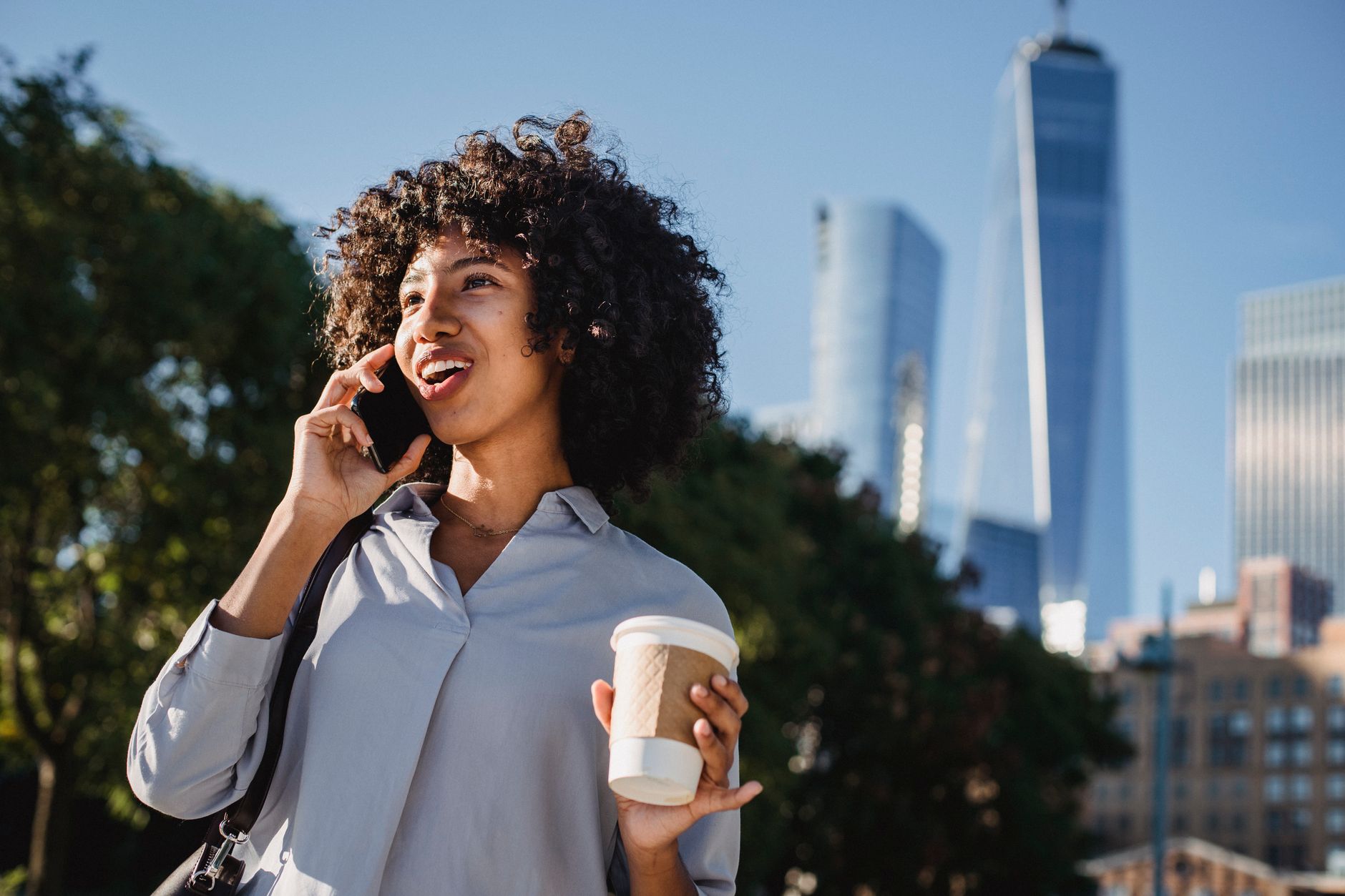 Woman enjoying coffee and a phone call with a city skyline backdrop.