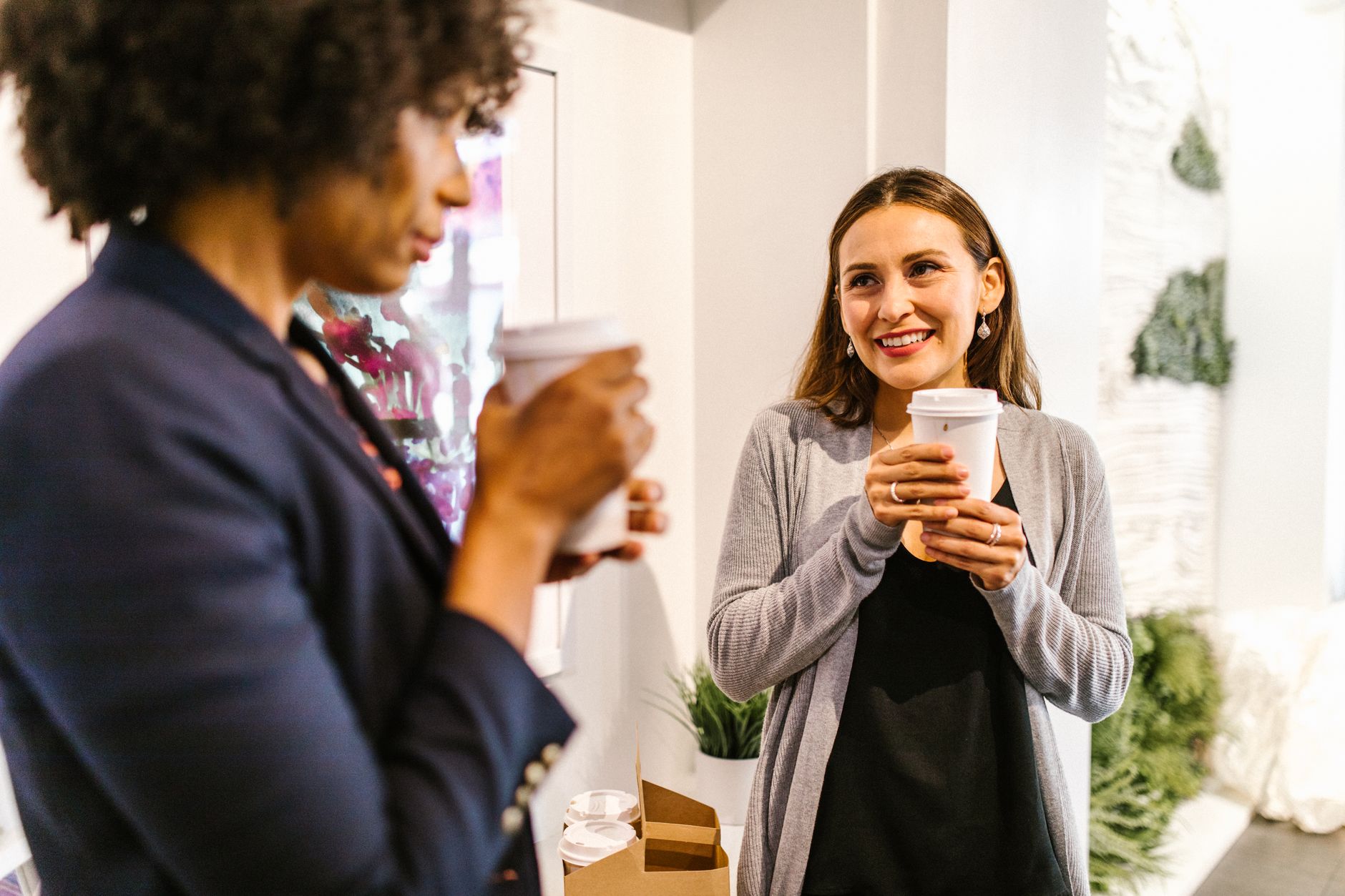 Two women having a conversation over coffee in a modern office setting.