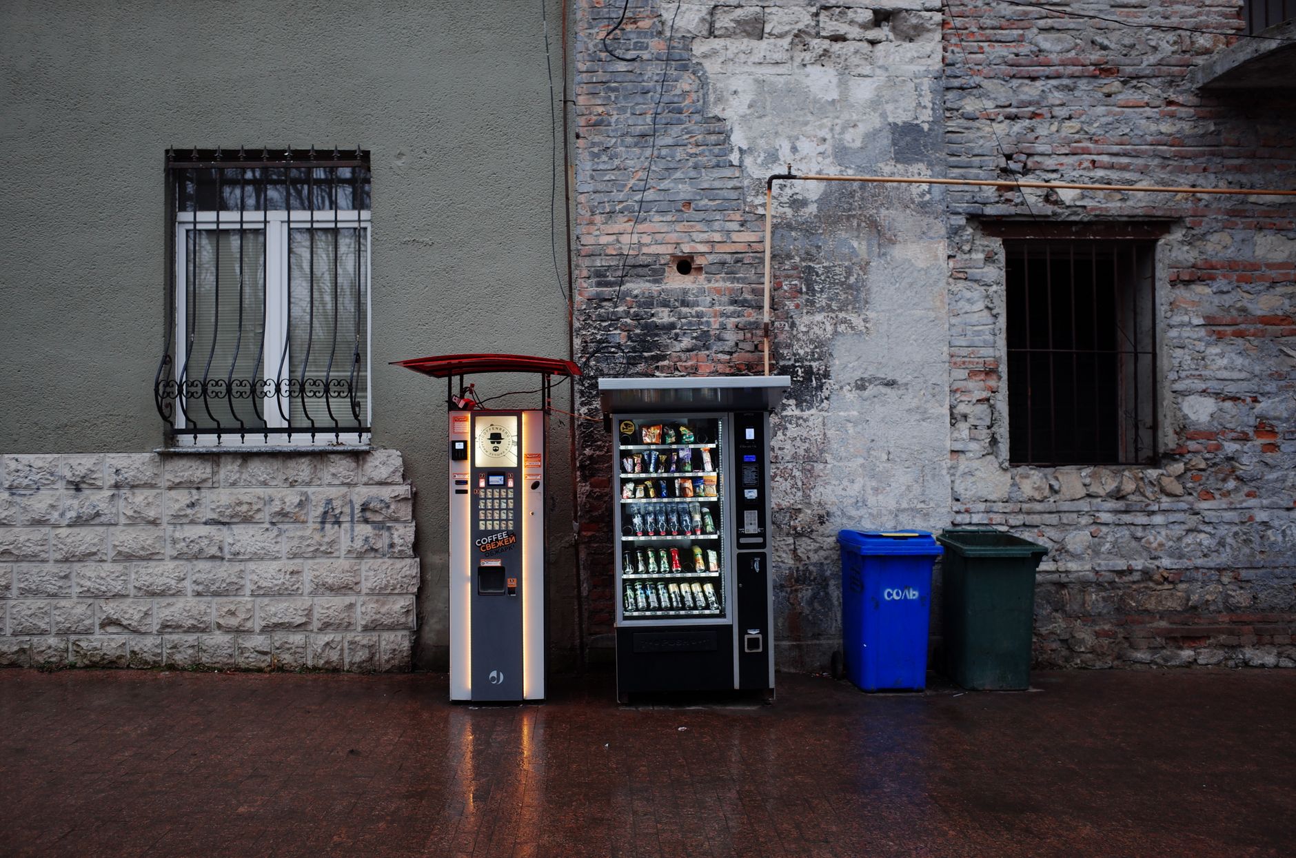Vending machines and trash bins against an urban stone wall backdrop.